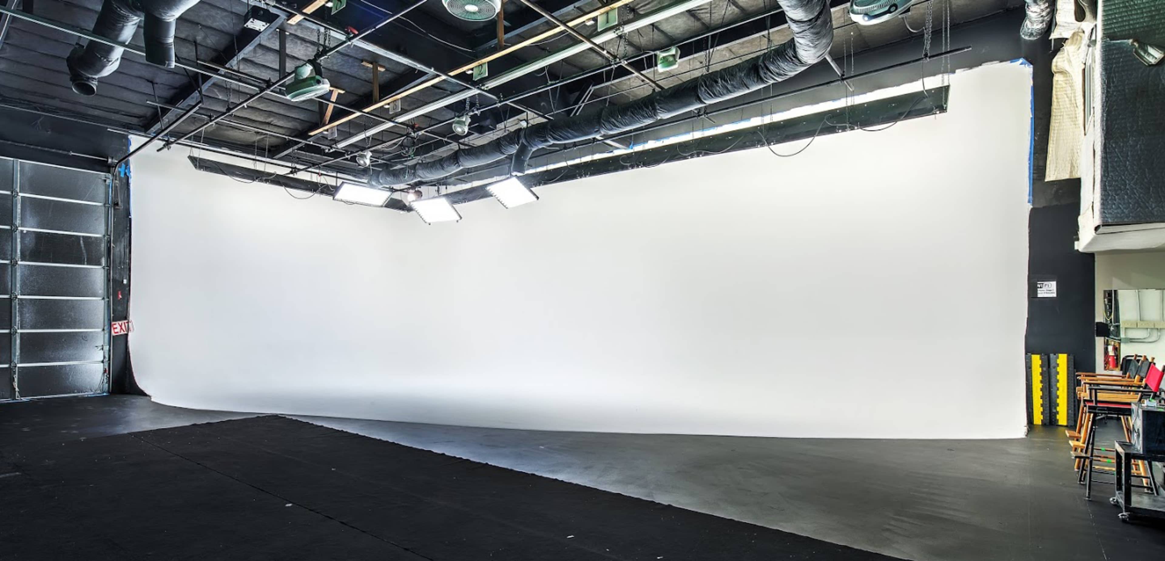 A spacious photography studio with a large white backdrop and studio lights mounted on the ceiling.