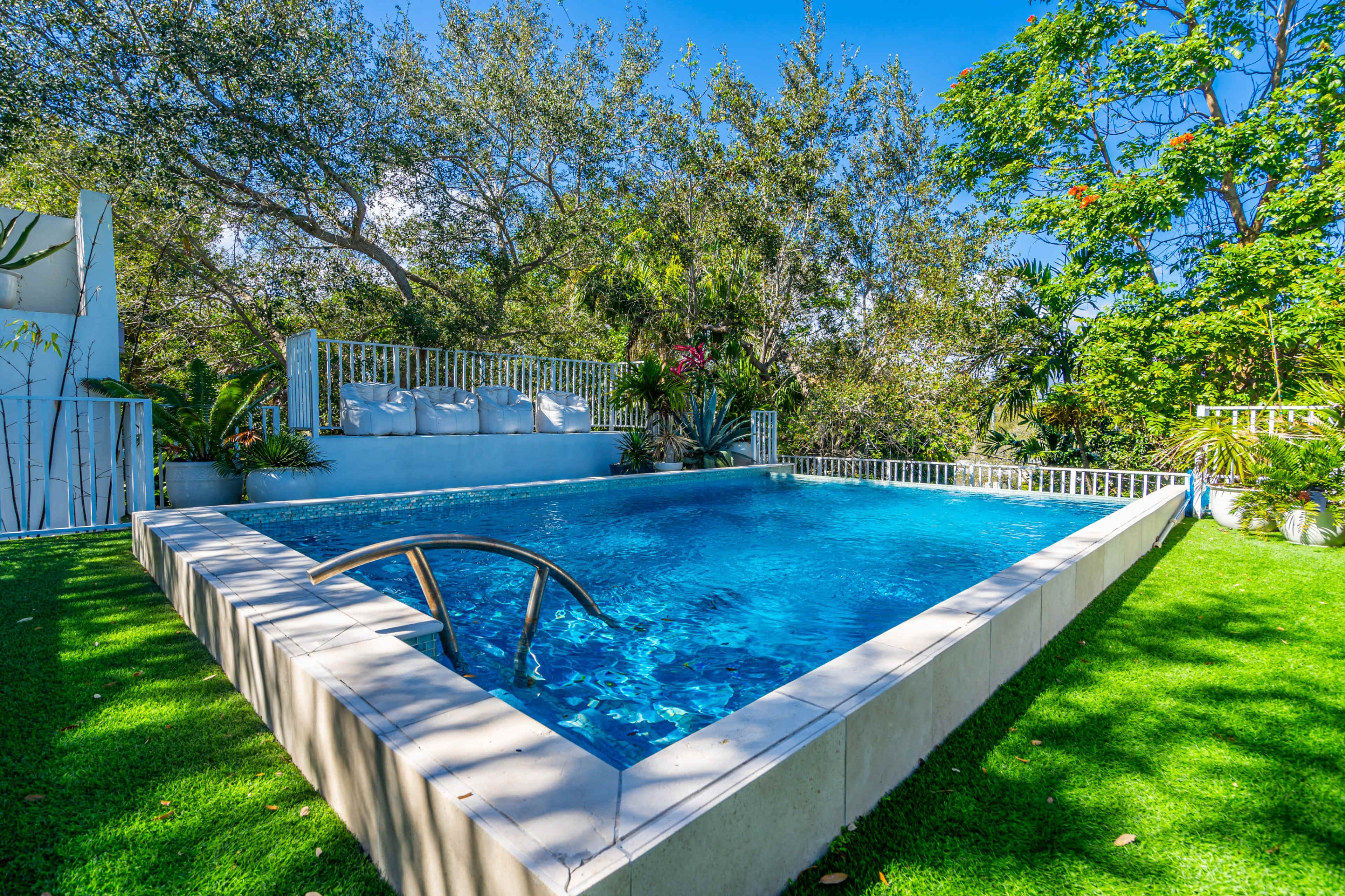 A rectangular swimming pool surrounded by lush greenery and a seating area on a raised platform.
