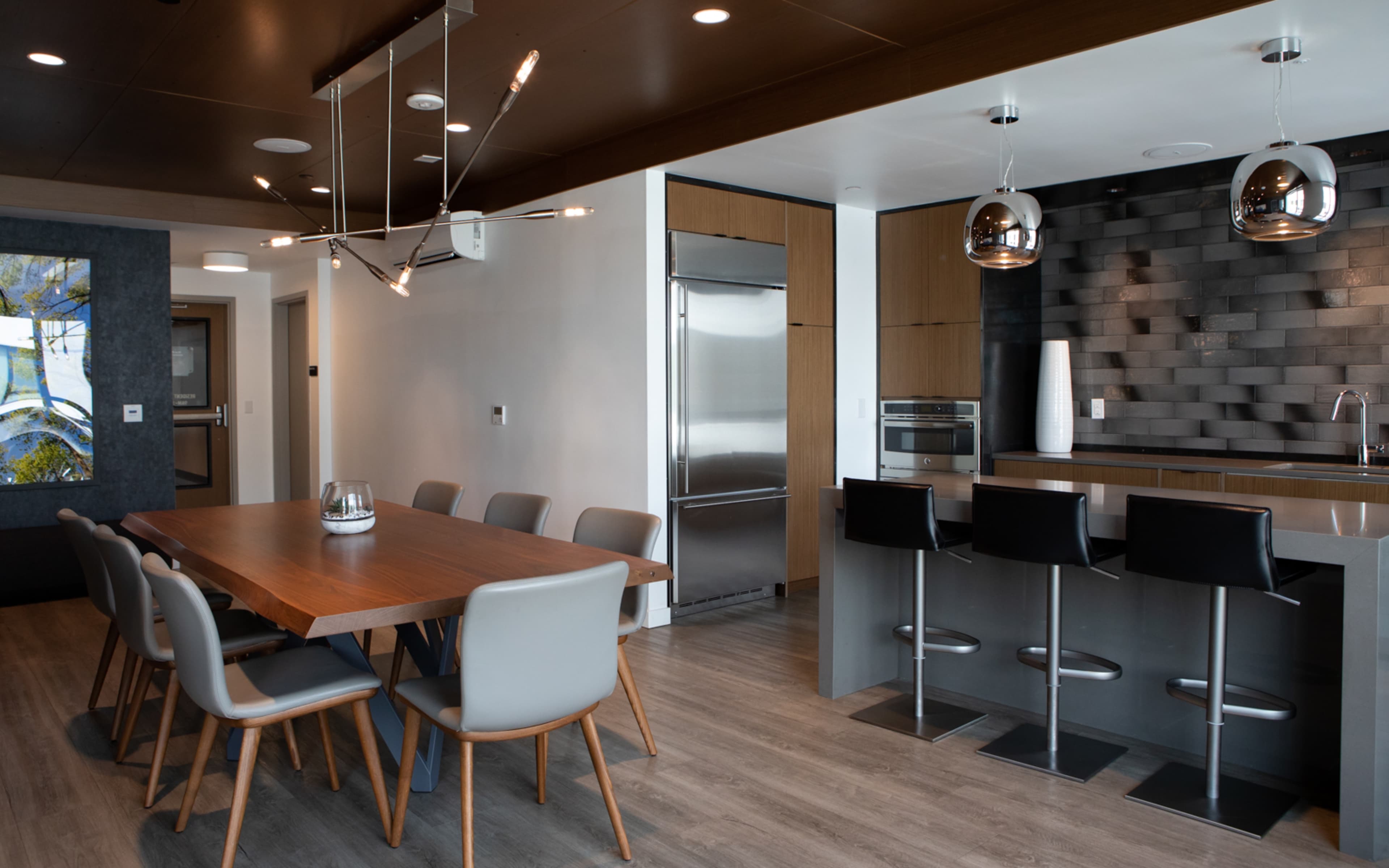 A modern kitchen and dining area featuring a wooden dining table with eight chairs, a sleek kitchen island with bar seating, and stainless steel appliances.
