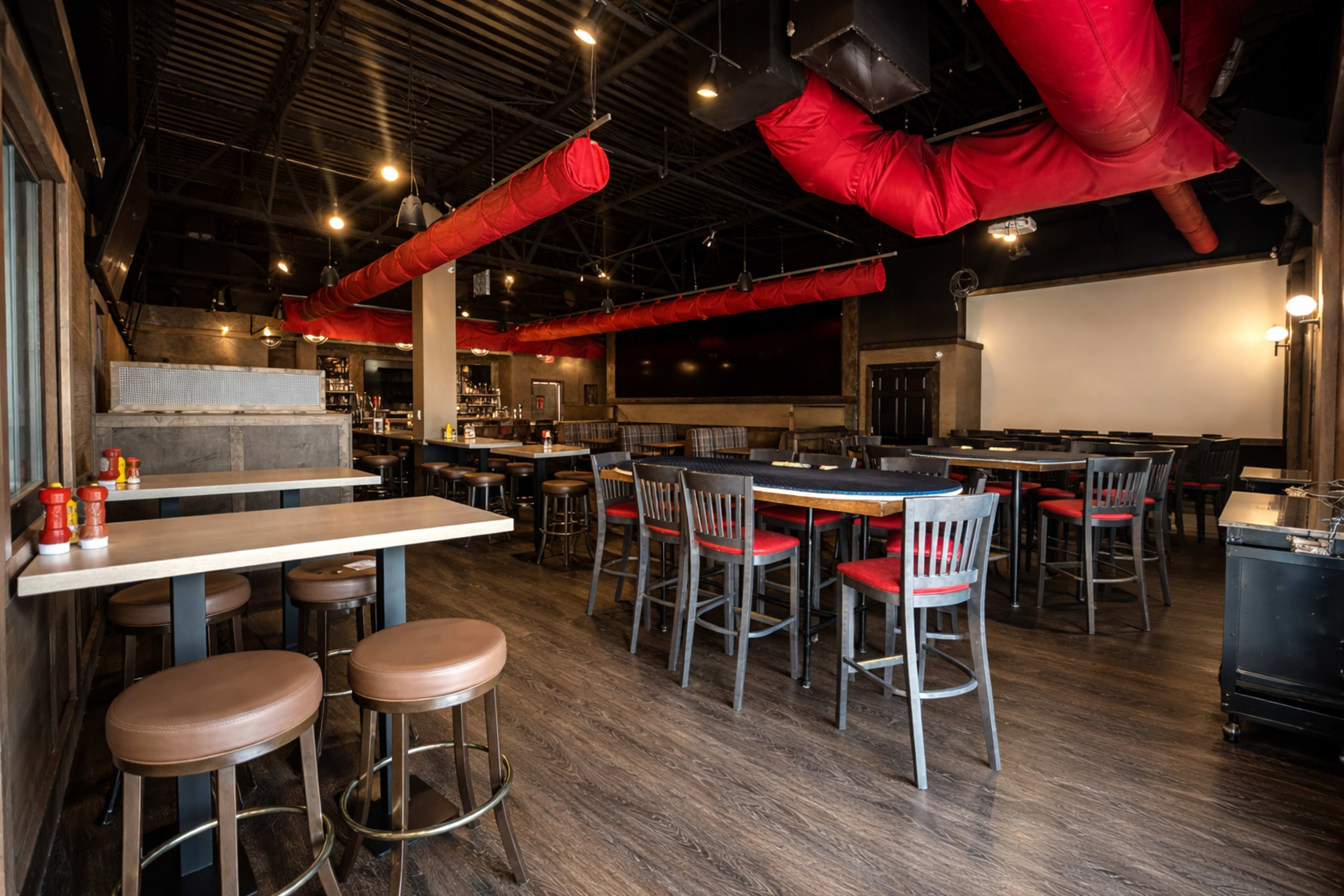 The image depicts an empty restaurant interior with rows of tables and chairs, a bar area, and red ductwork overhead.