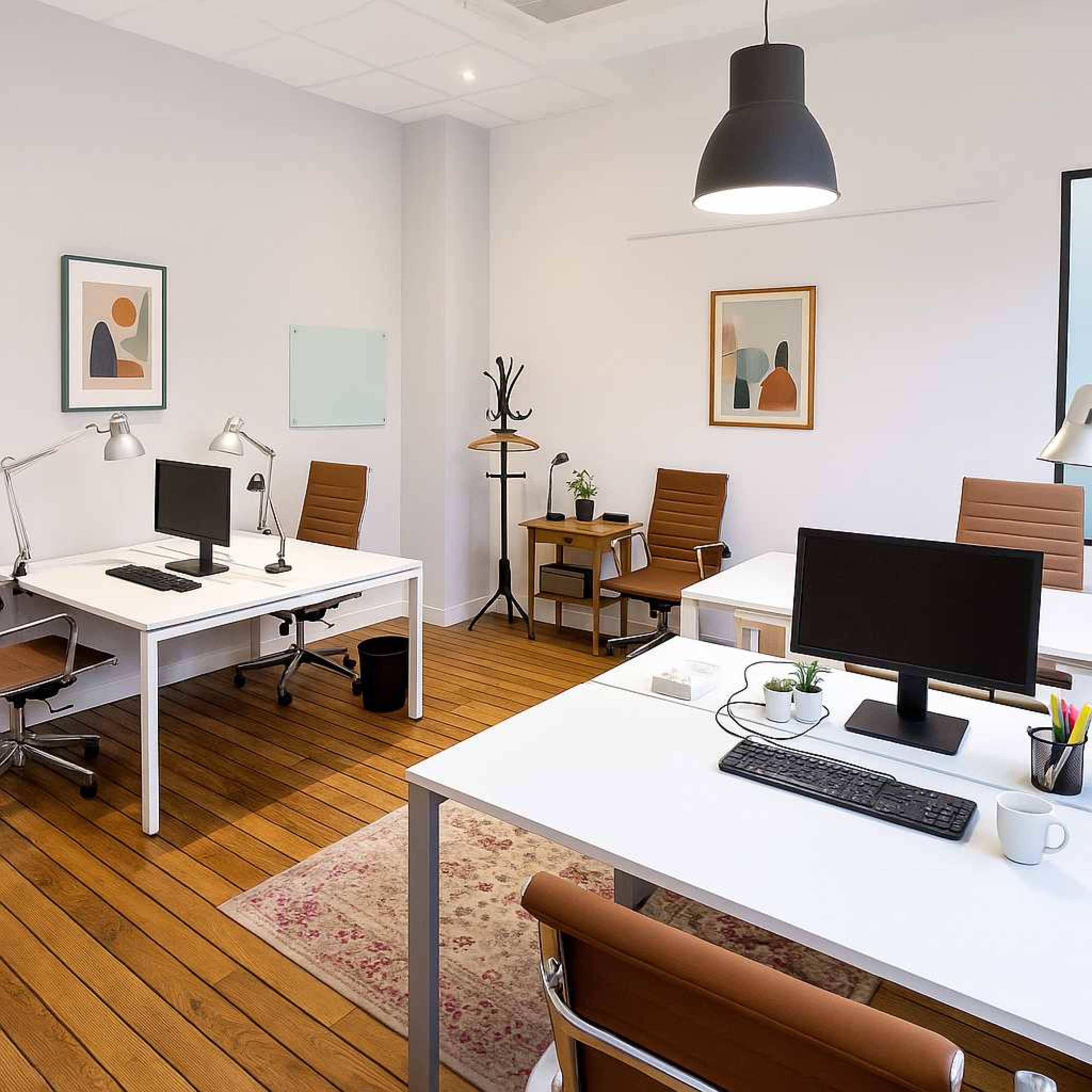 The image shows a modern office space featuring two white desks with computer monitors, wooden flooring, and minimalistic decor items, including plants and artwork.