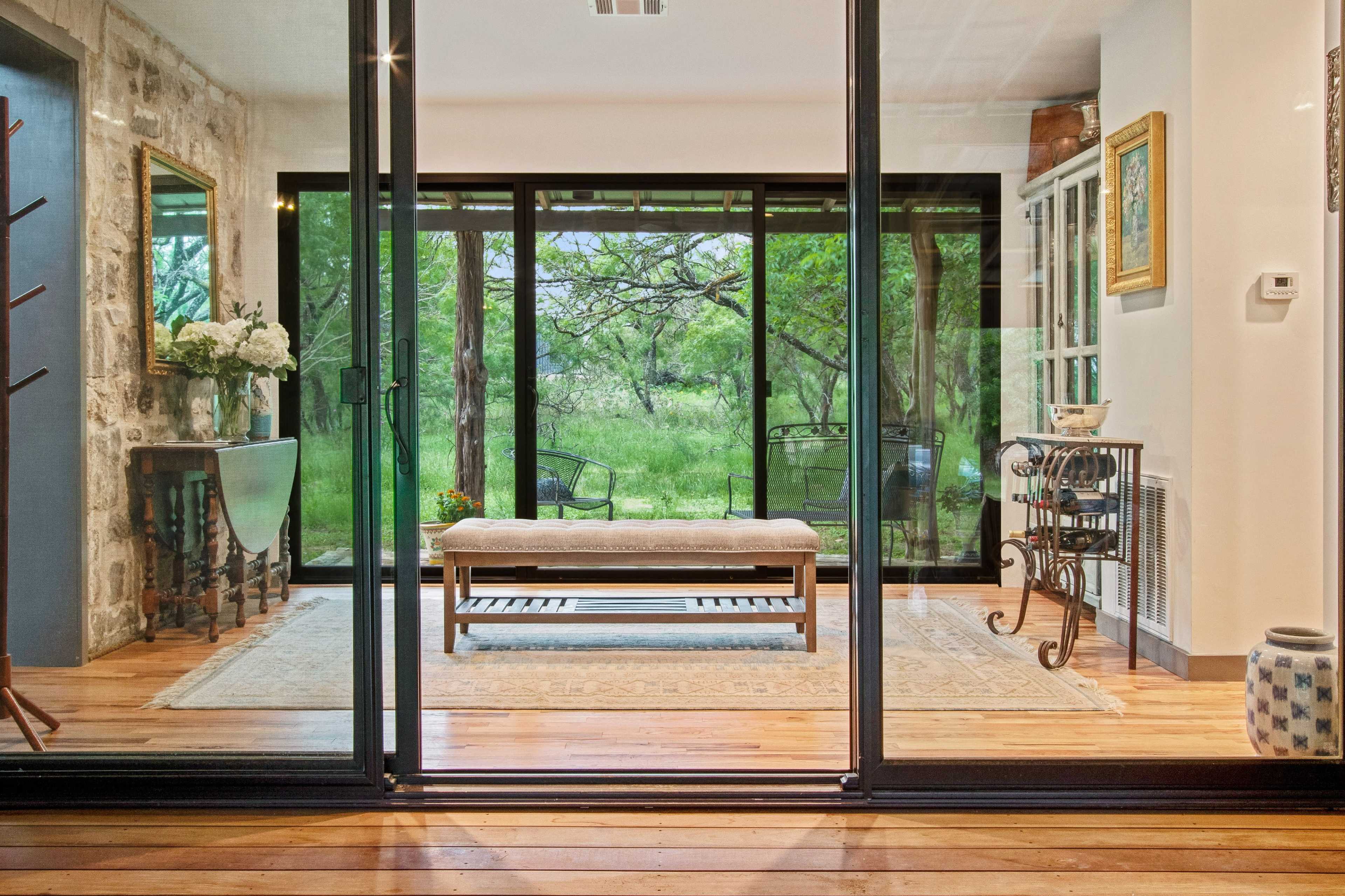 A spacious room opens to a lush outdoor view through large glass doors, featuring wooden flooring and a central bench.