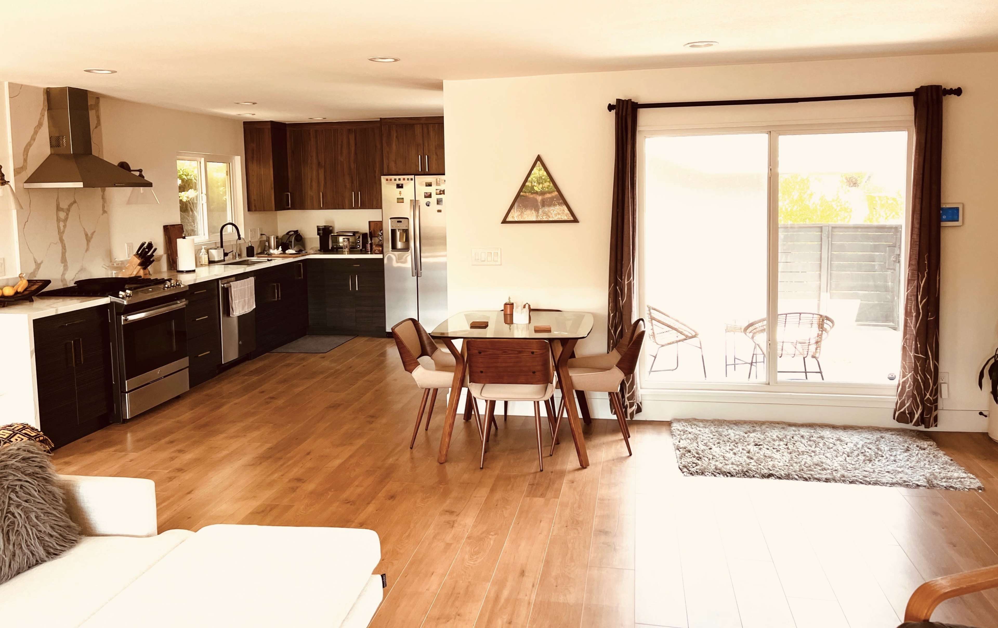 A modern kitchen and dining area with wooden floors, featuring a dining table set for four, and an adjacent living space with a white couch.