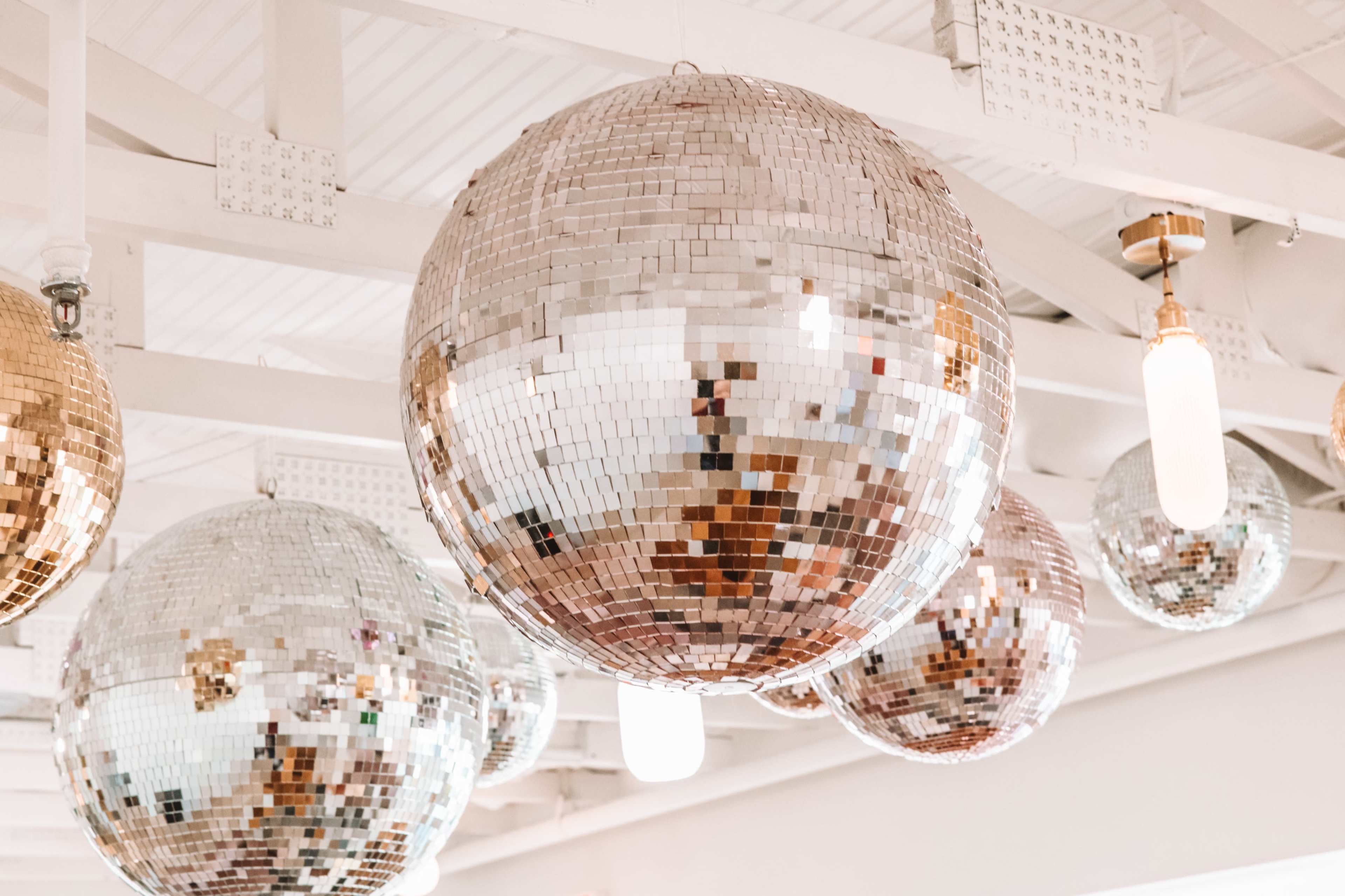 Several large disco balls hanging from a ceiling with white beams.
