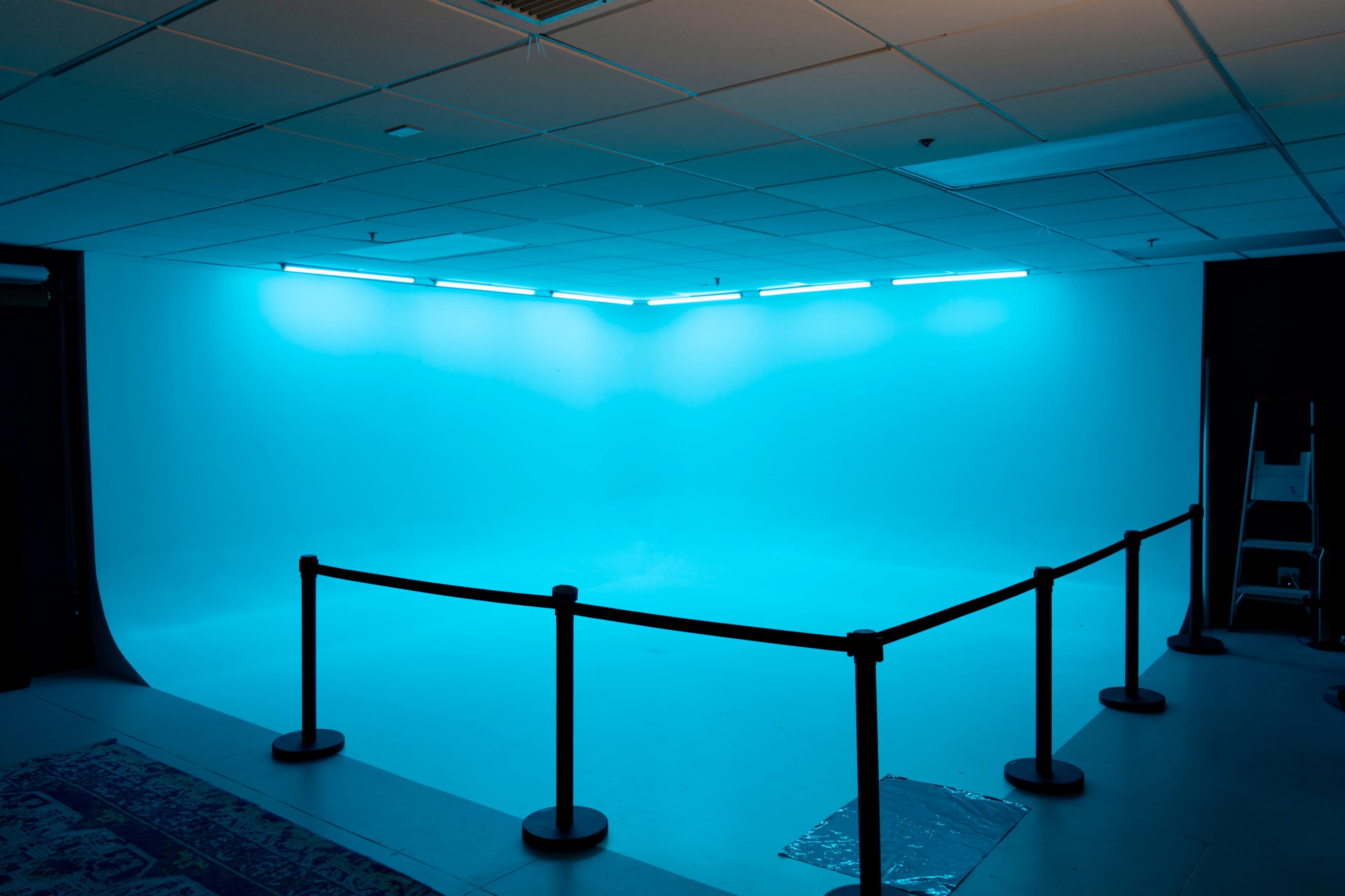 The image shows a vacant photography studio with a blue backdrop and a barrier rope surrounding the area.