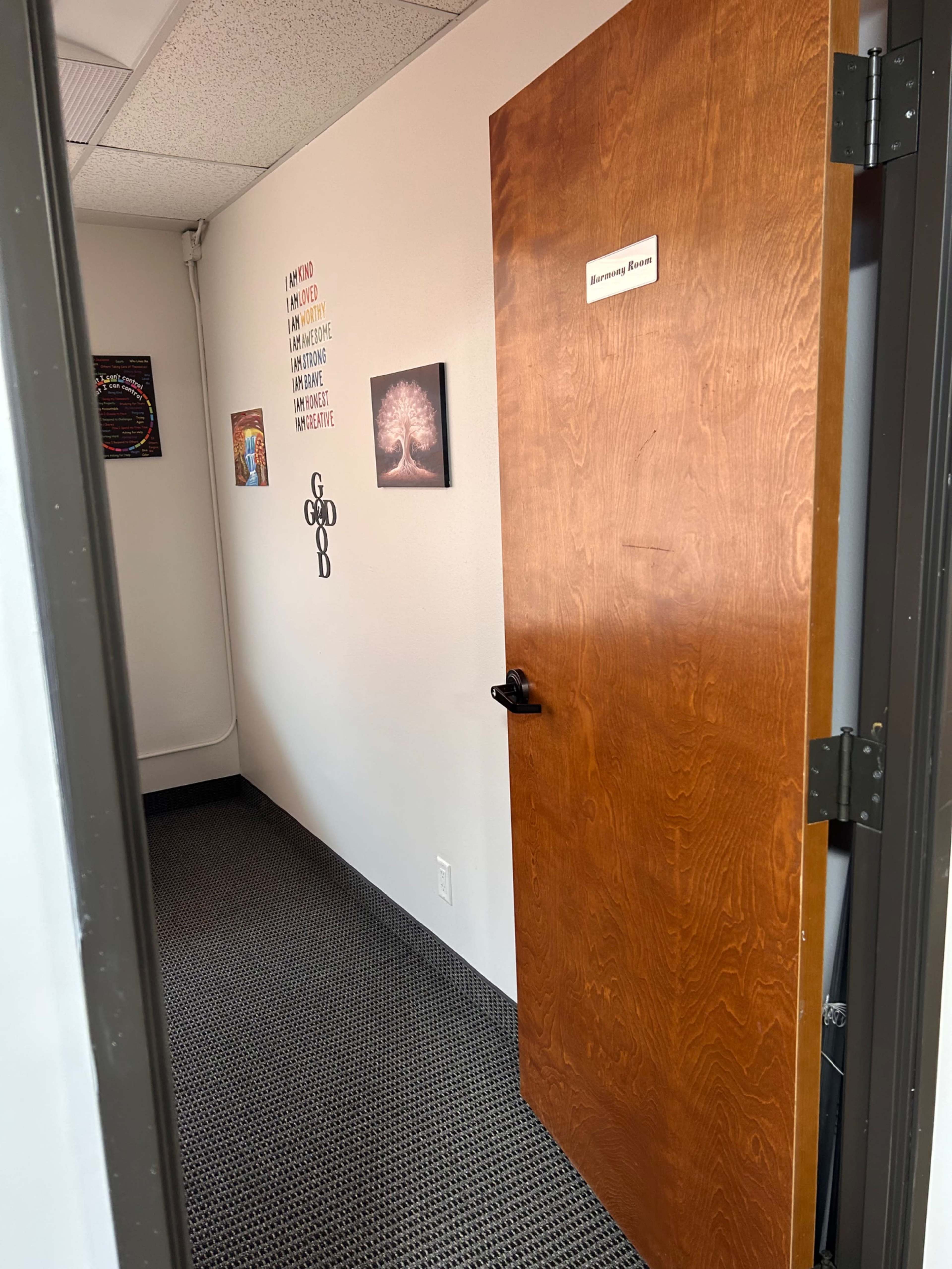 A brown wooden door opens into a hallway with framed artwork and motivational quotes on the walls.