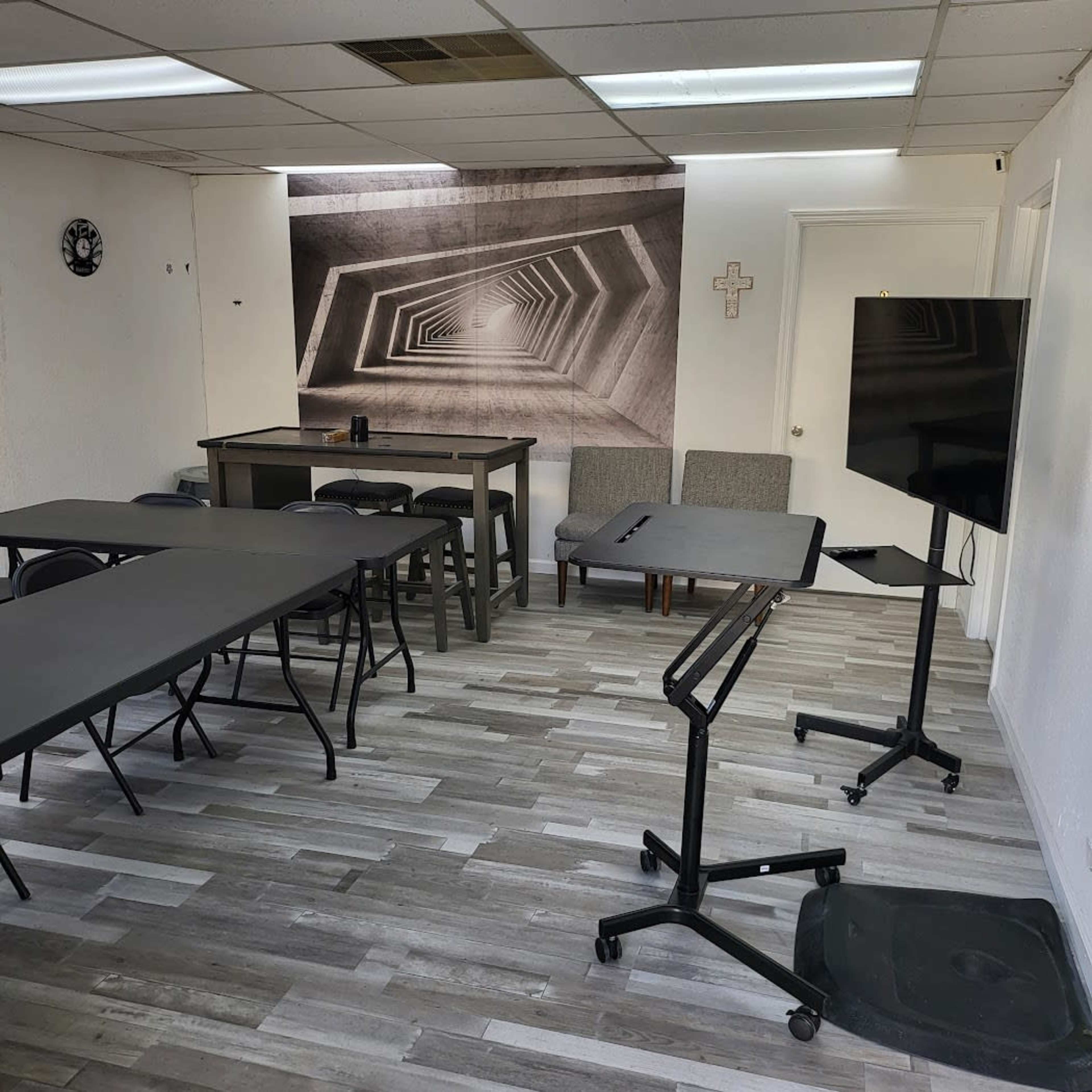 A modern meeting room with several folding tables, chairs, and a large wall mural of a geometric pattern.