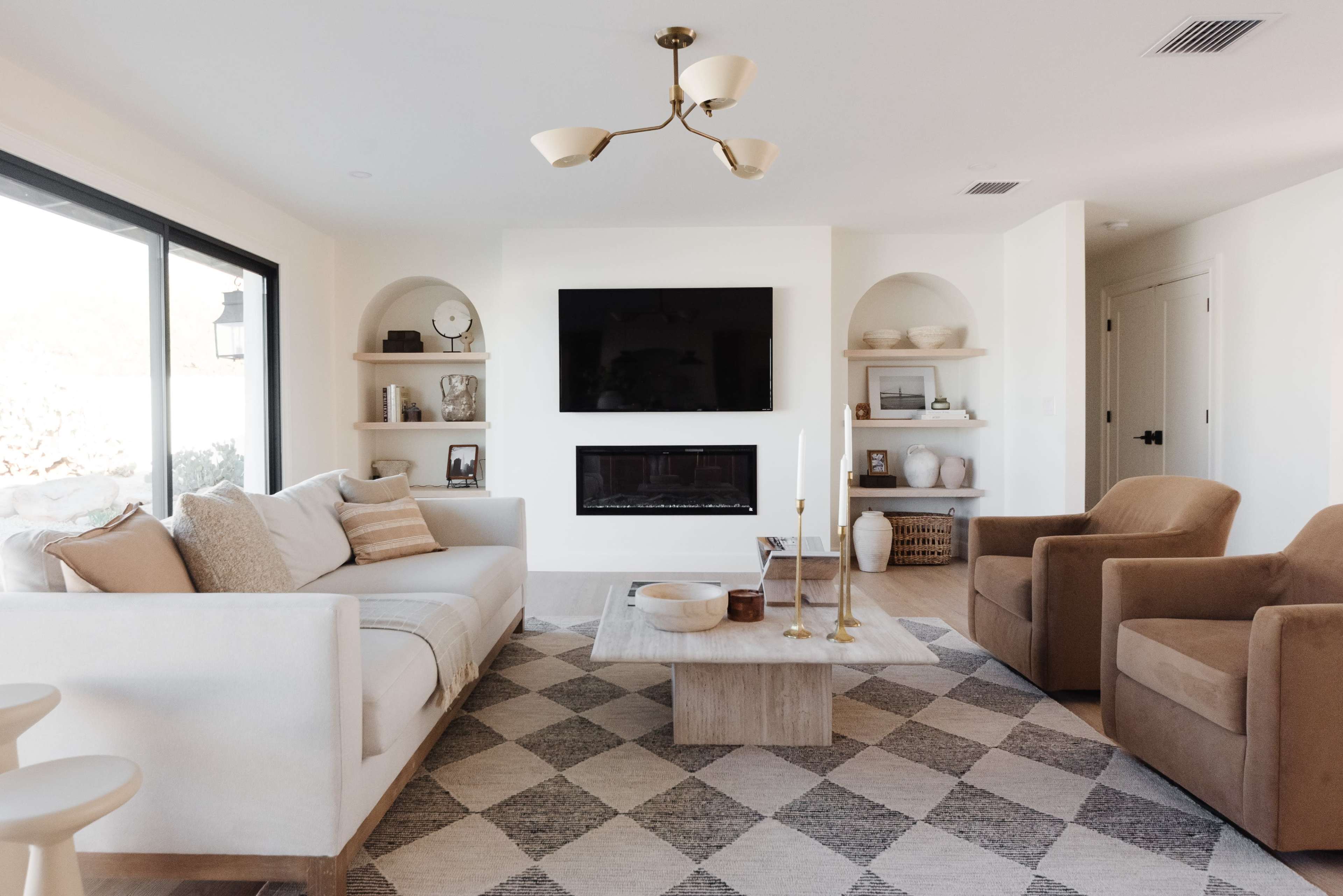 The living room features a sofa, two armchairs, a coffee table, and shelves with decorative items, all arranged around a modern fireplace.