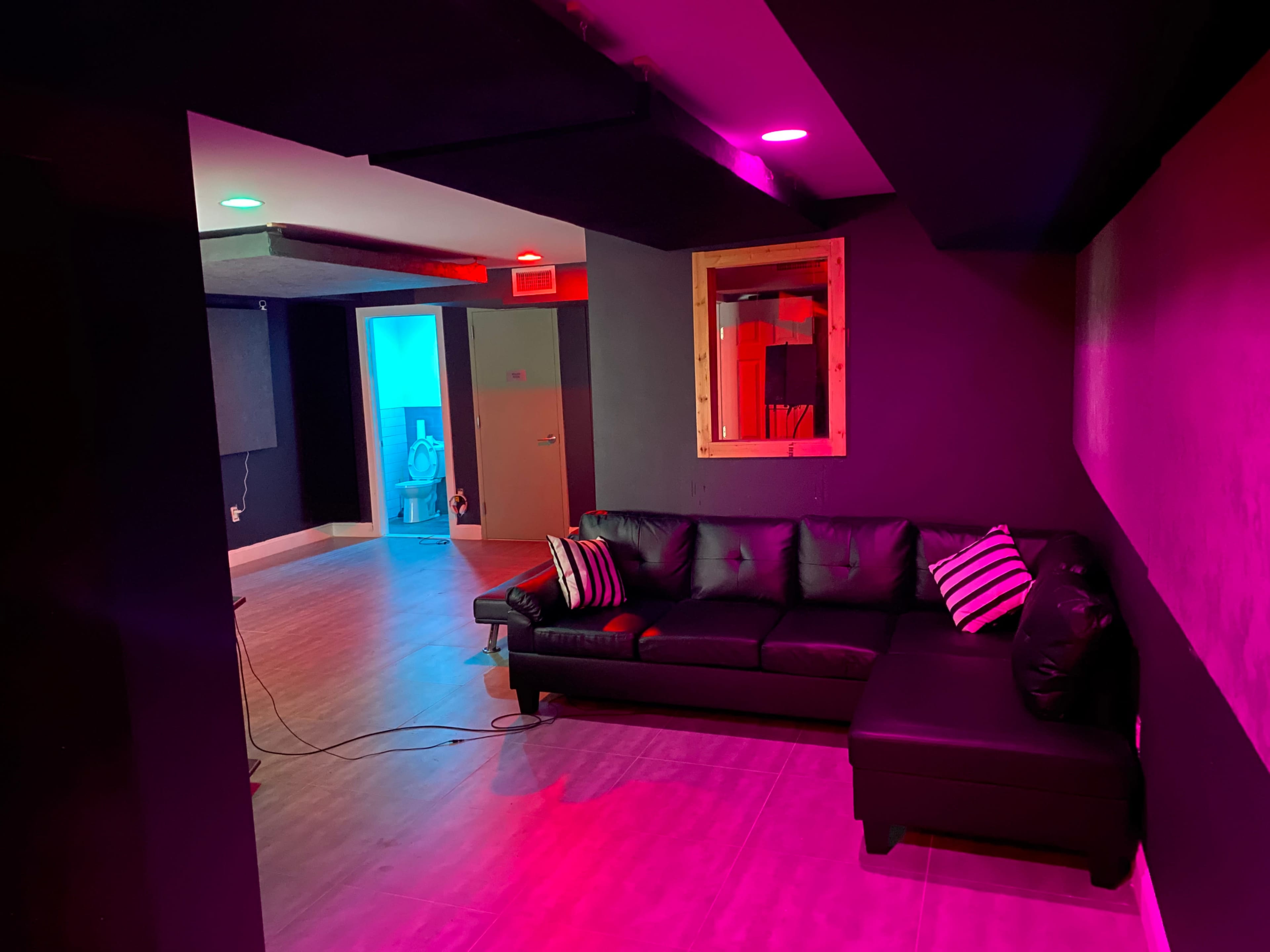 A modern lounge area with a black leather couch facing a doorway, illuminated by colored lights.