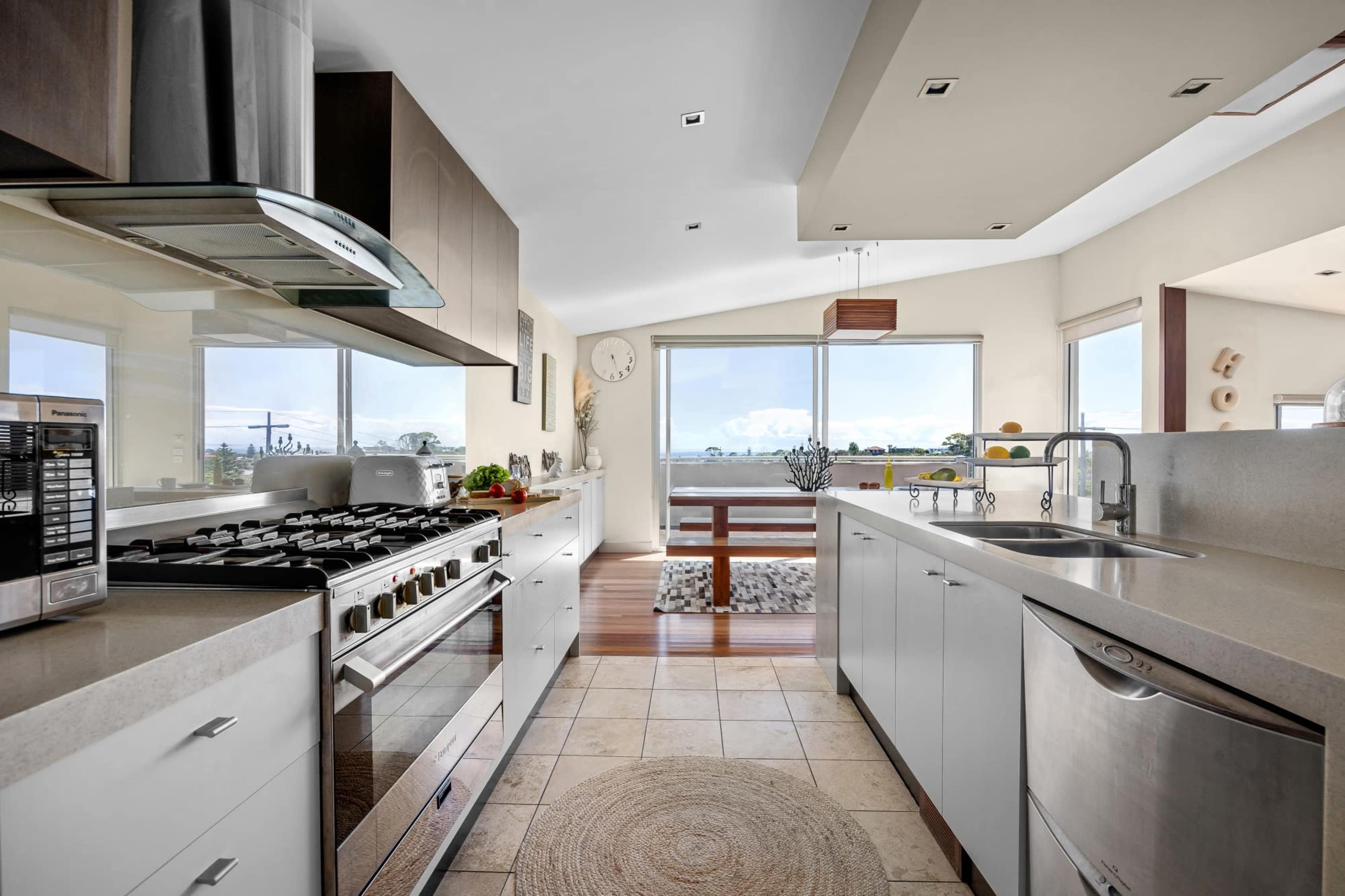 A modern kitchen features stainless steel appliances, light-colored cabinetry, and large windows offering a view of the outdoors.