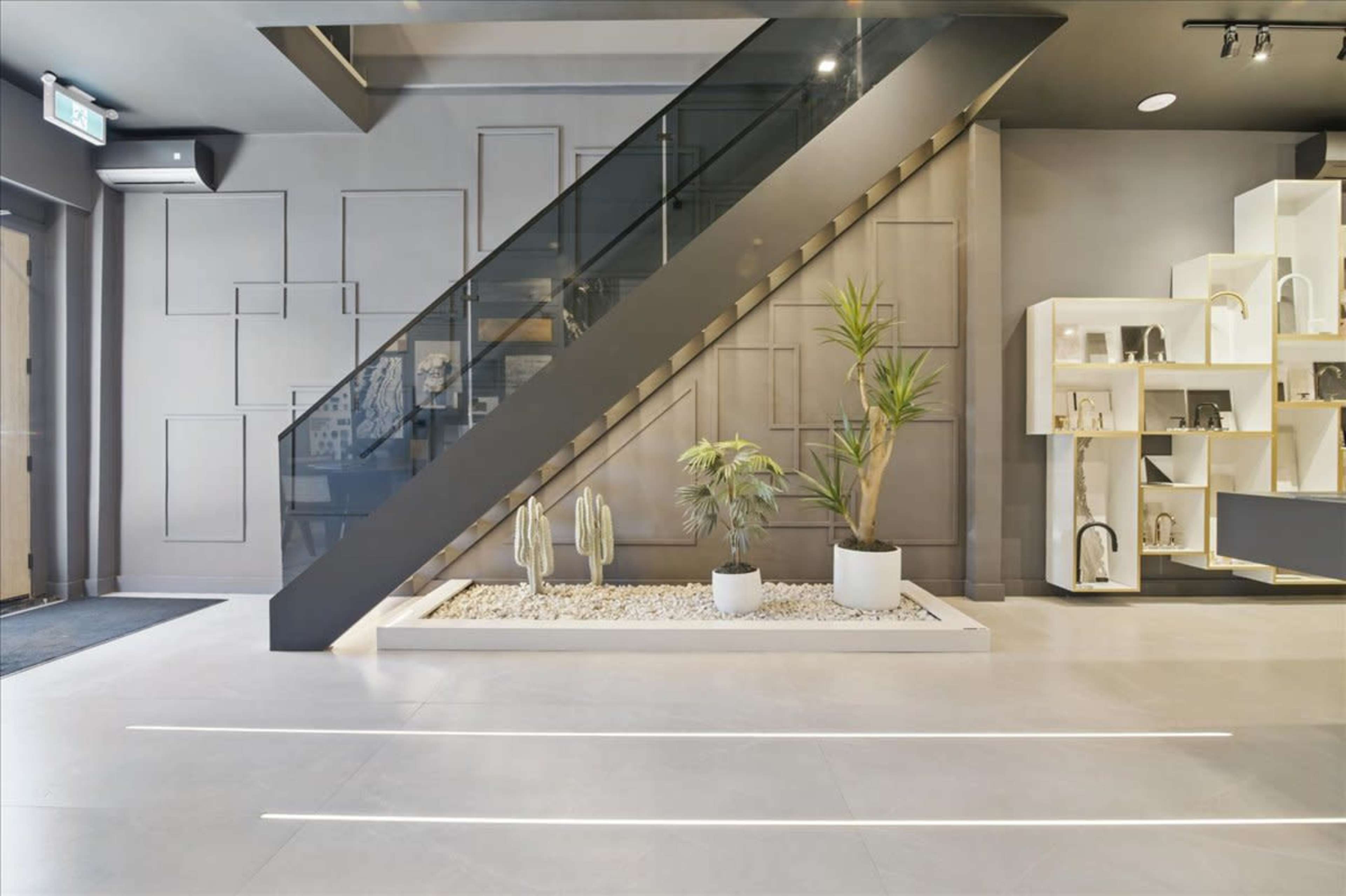 The image features a modern interior with a glass staircase, planters, and a minimalistic shelving unit against a gray wall.