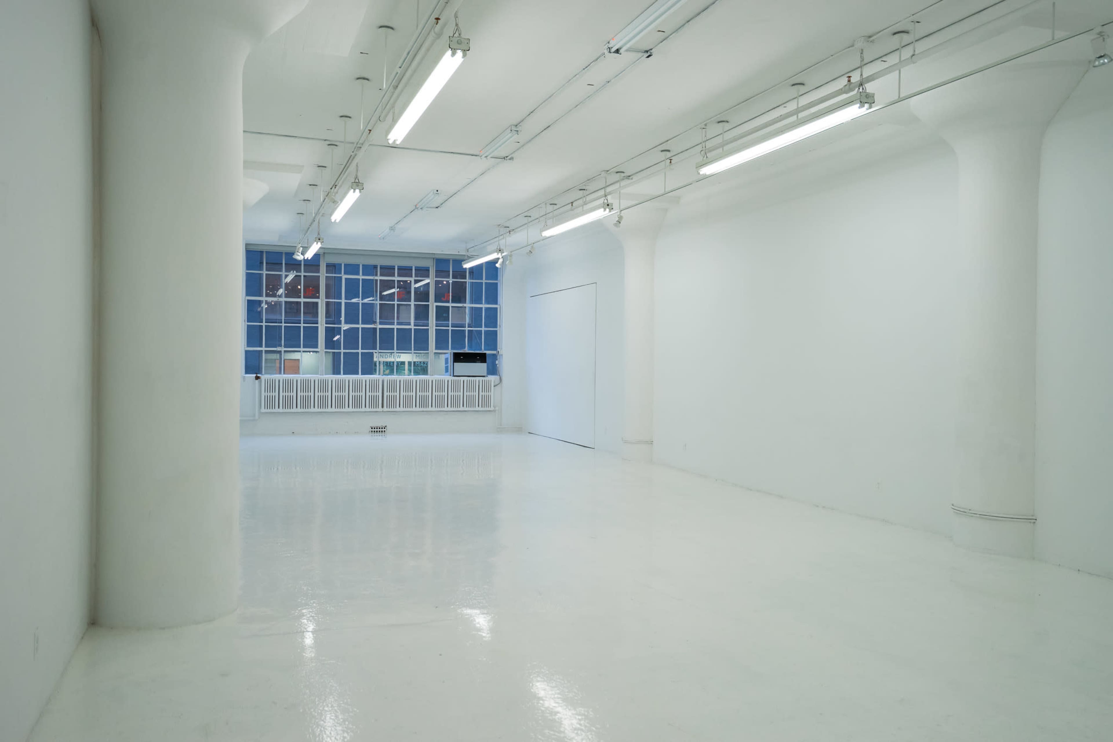 The image shows a spacious, empty room with white walls, a polished floor, and large windows.