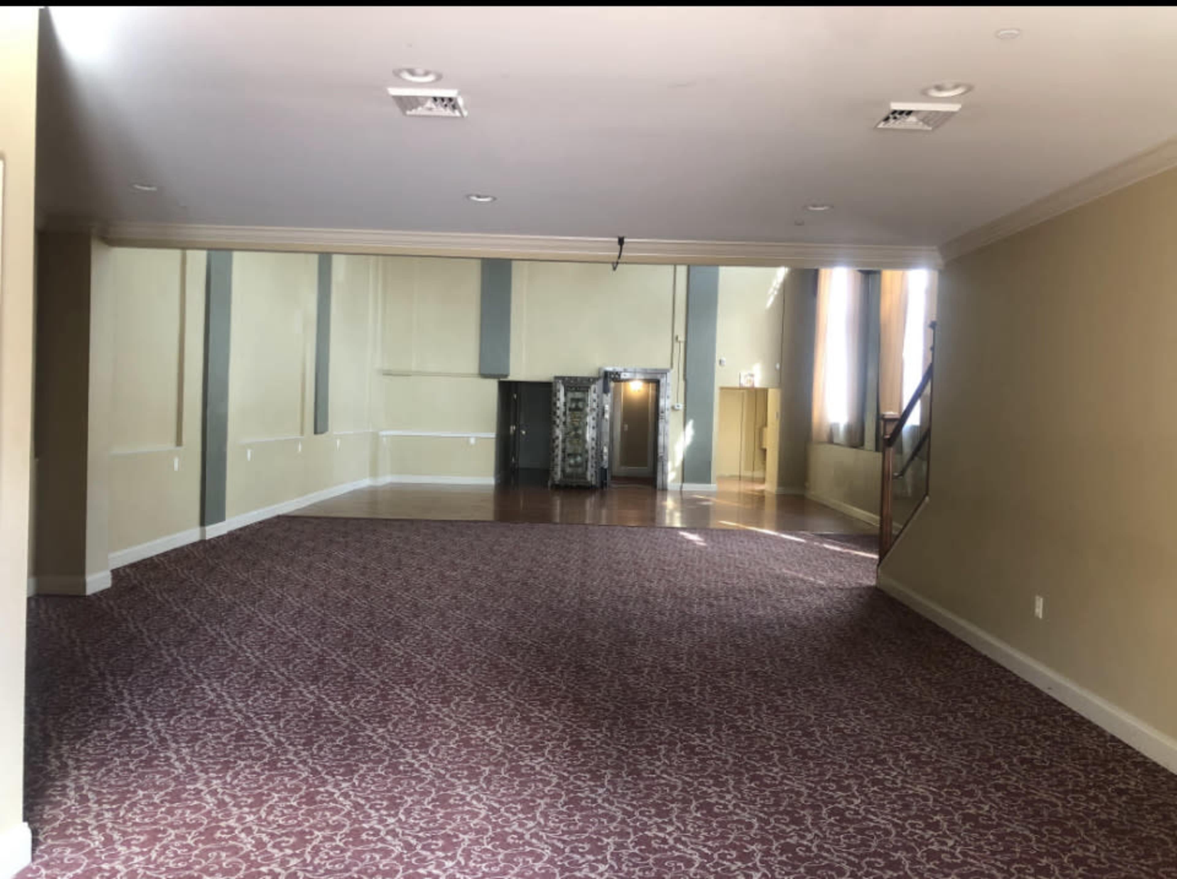 An empty room with beige walls, patterned carpet, and a staircase on one side leading to another level.