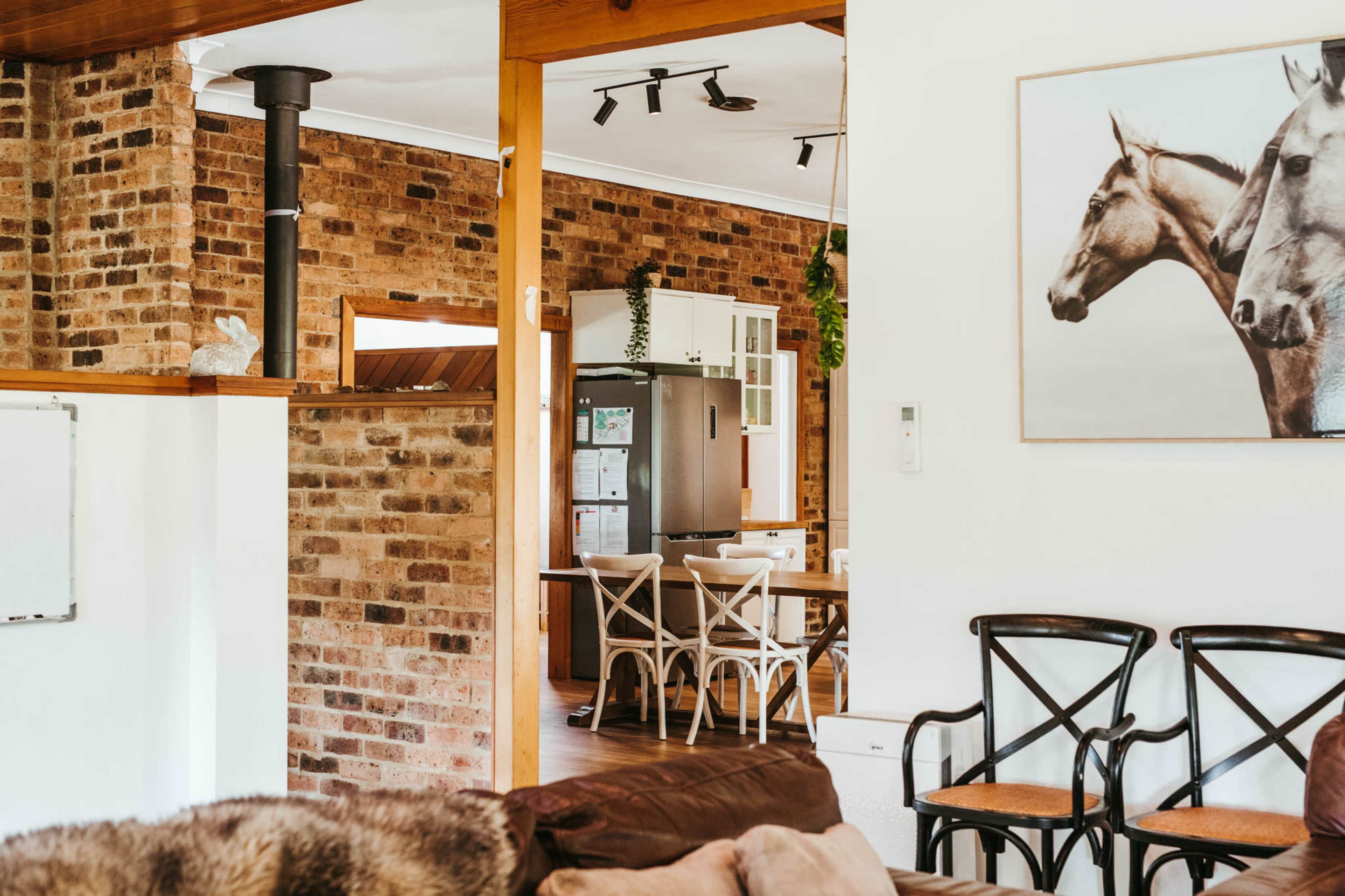 A cozy interior space with exposed brick walls, featuring a living area with wooden furniture and an adjacent kitchen area visible in the background.