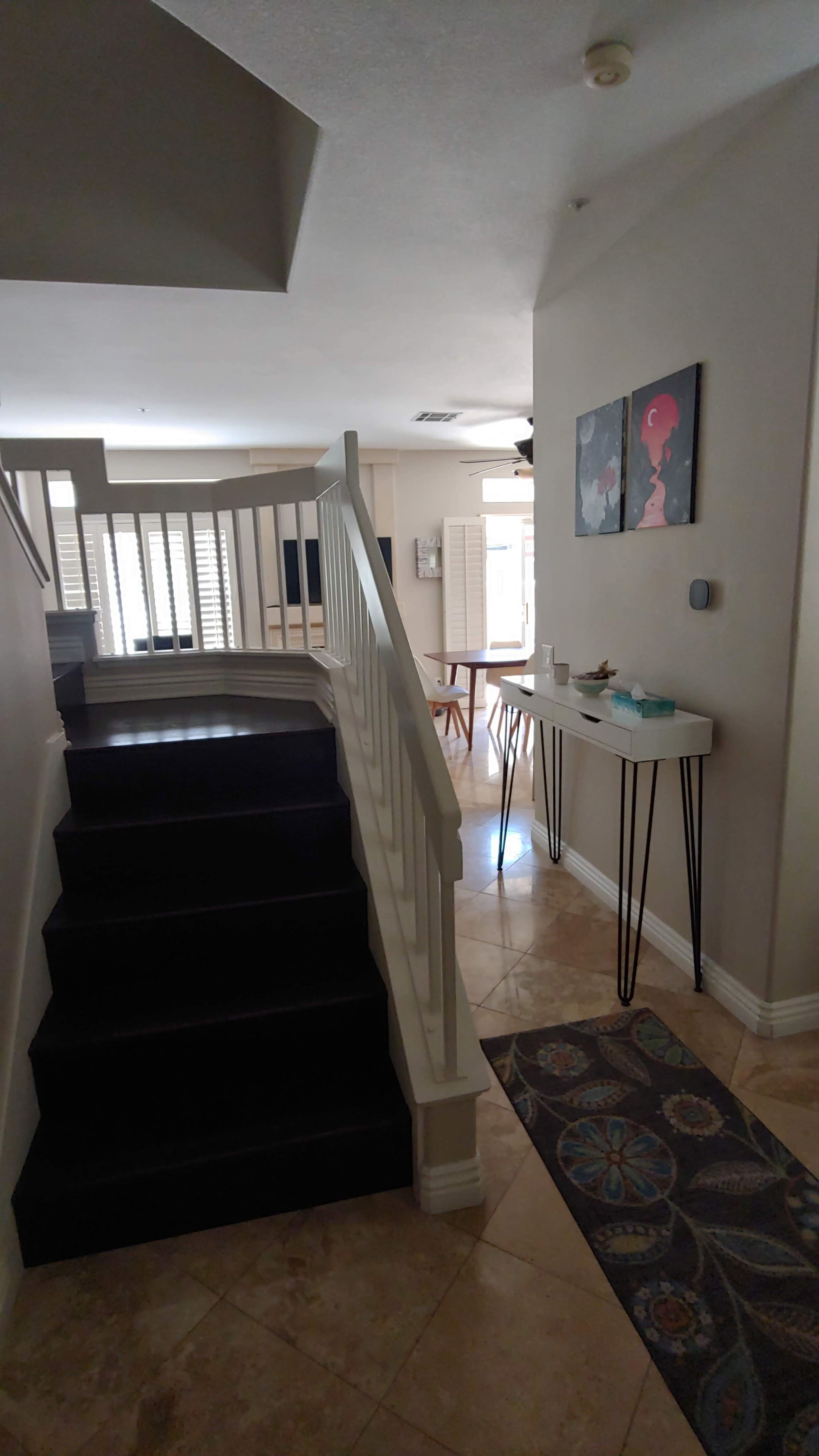 A staircase leading to an upper level in a home, with a small console table and a patterned rug on the tiled floor near the entrance.