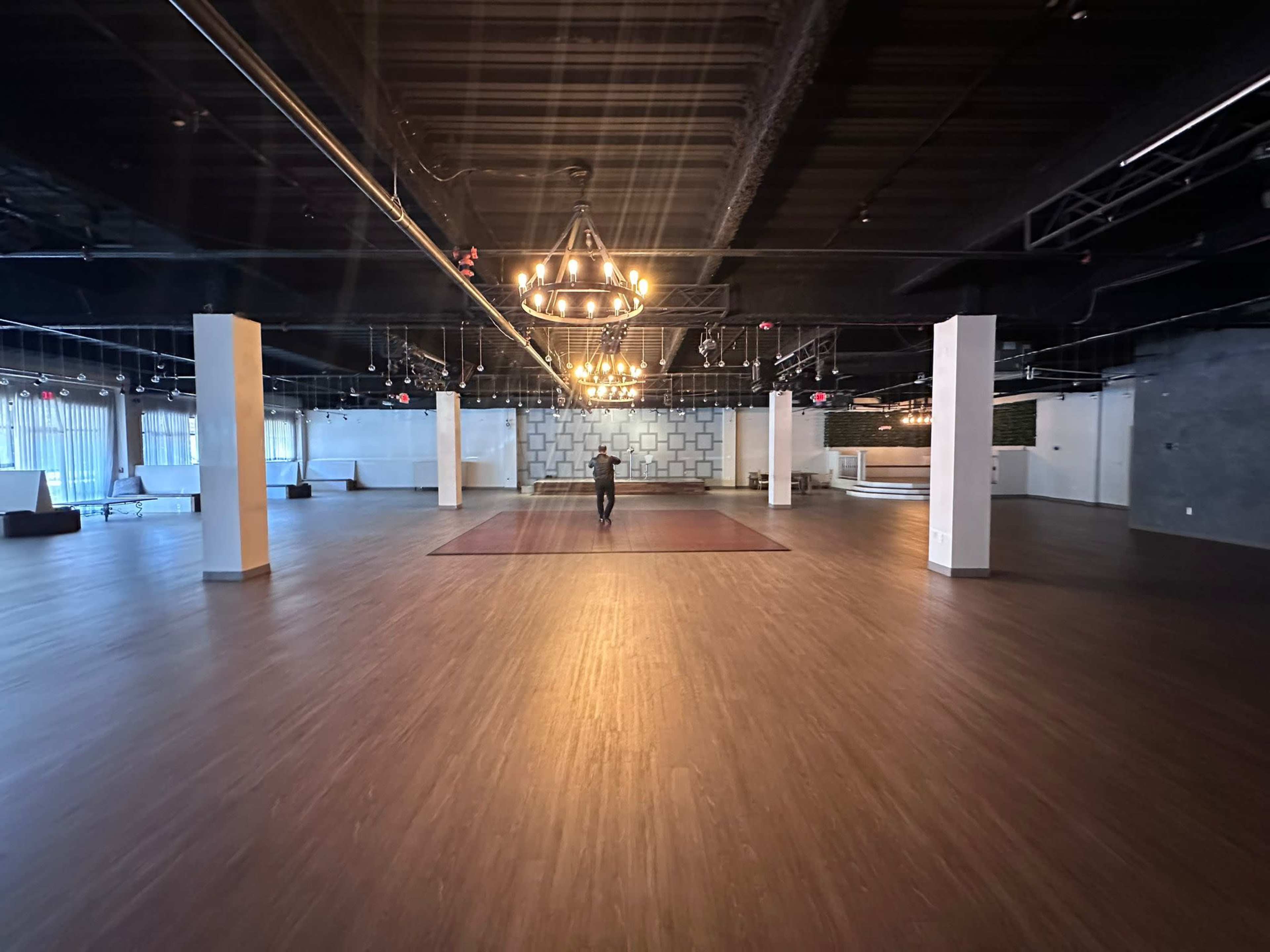 A person walks across a spacious, empty event hall with wooden flooring and decorative lighting.