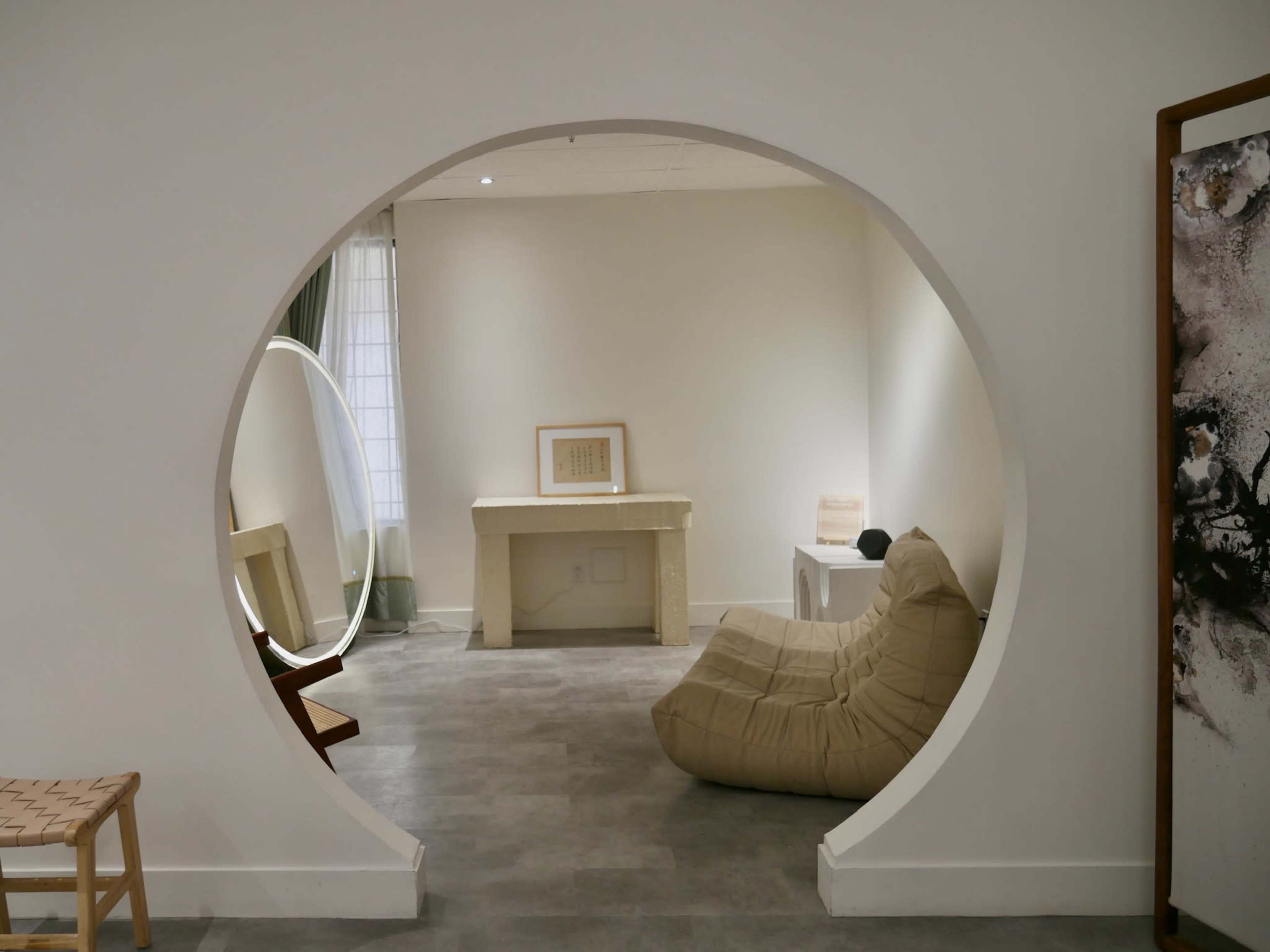 A circular opening frames a minimalist lounge area featuring a bean bag chair and a stone table.