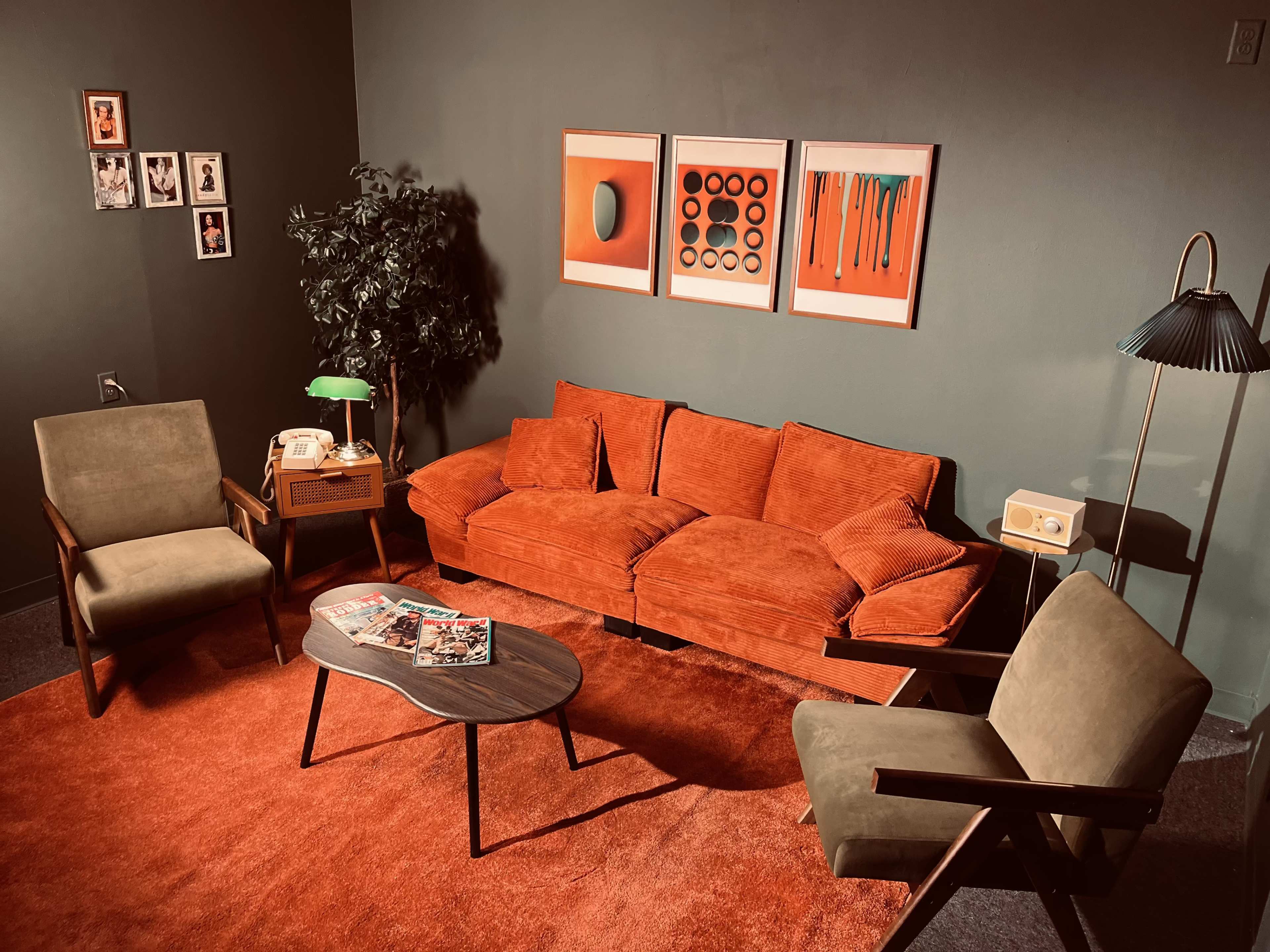 The image shows a retro-style living room with a bright orange sofa, two armchairs, a wooden coffee table, and framed artwork on the wall.