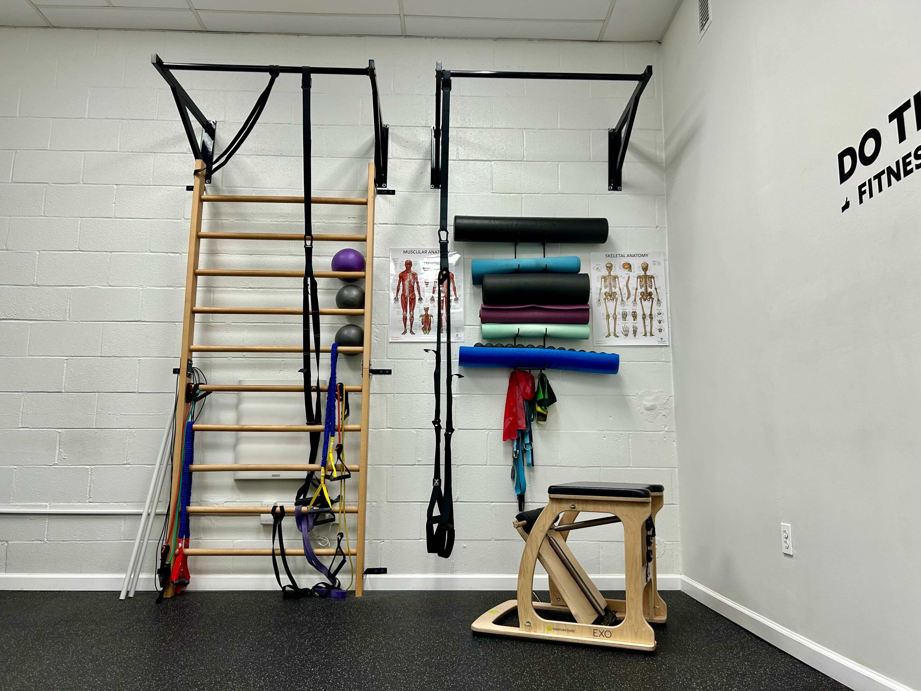 A fitness room equipped with a wooden climbing frame, various exercise tools, and instructional posters on the wall.