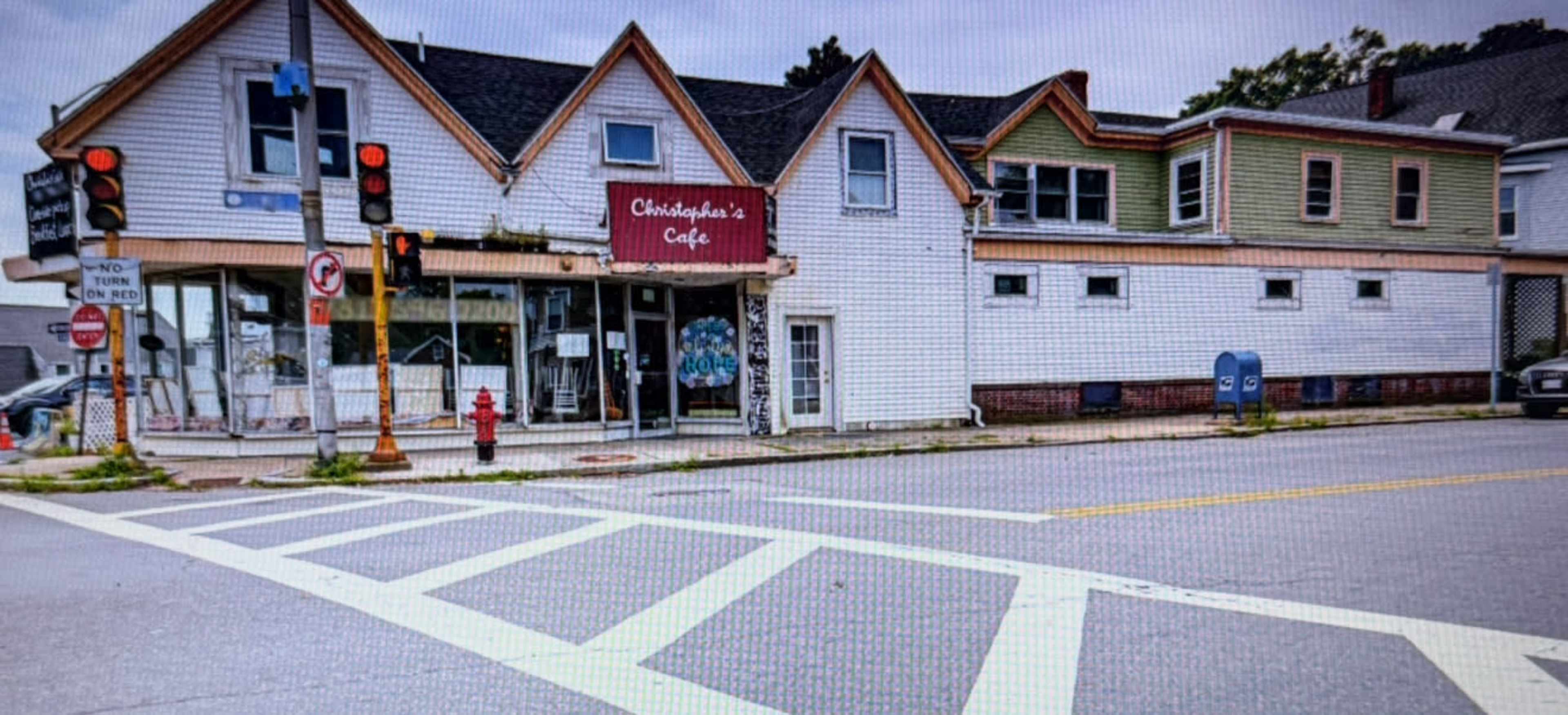 The image shows a quaint, multi-colored building with a café named "Christopher's Café" on the corner of a street, featuring traffic lights and a fire hydrant nearby.