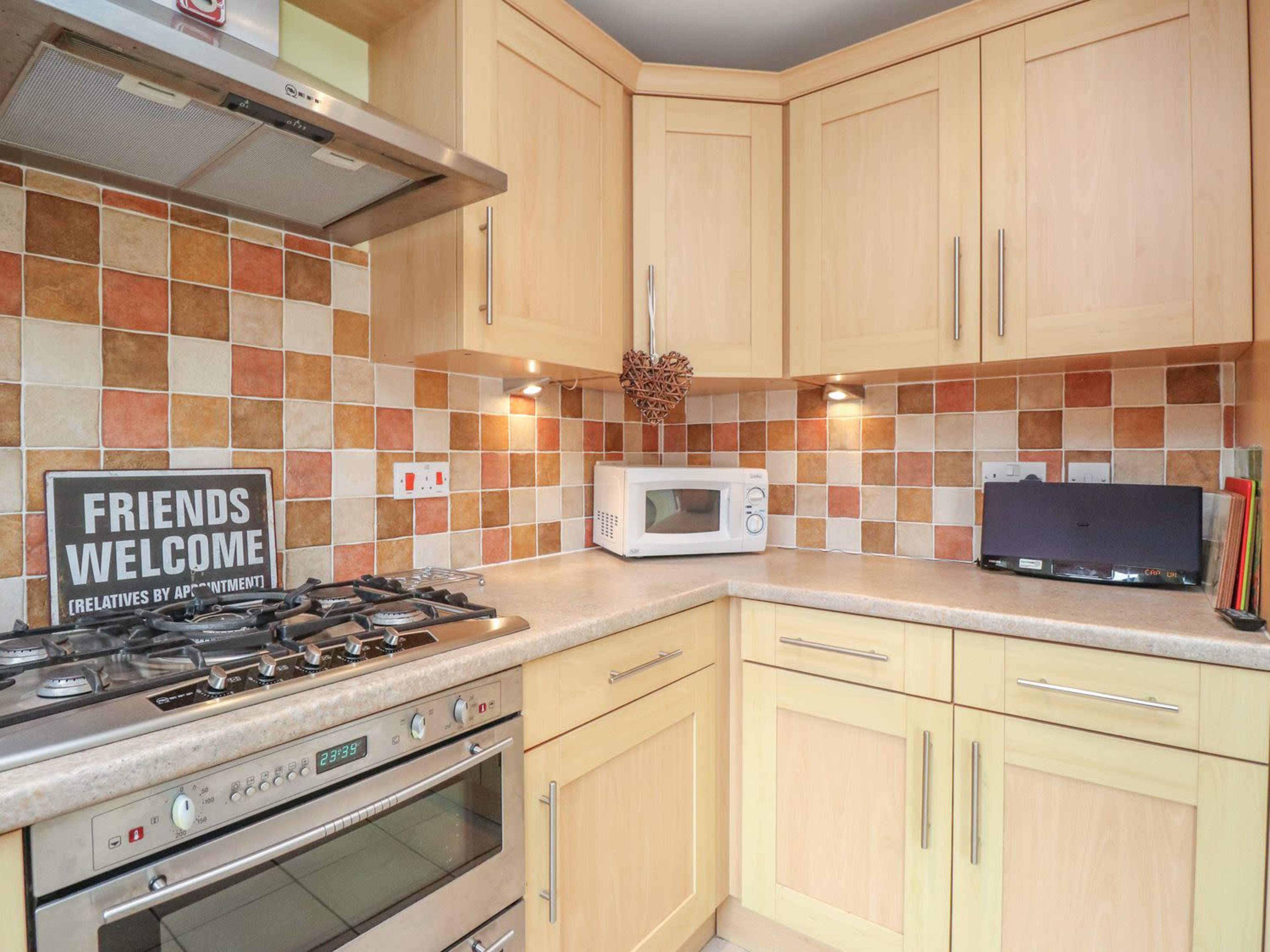 A kitchen with light wooden cabinets, a tiled backsplash in various colors, a gas stove, and a microwave on the countertop.