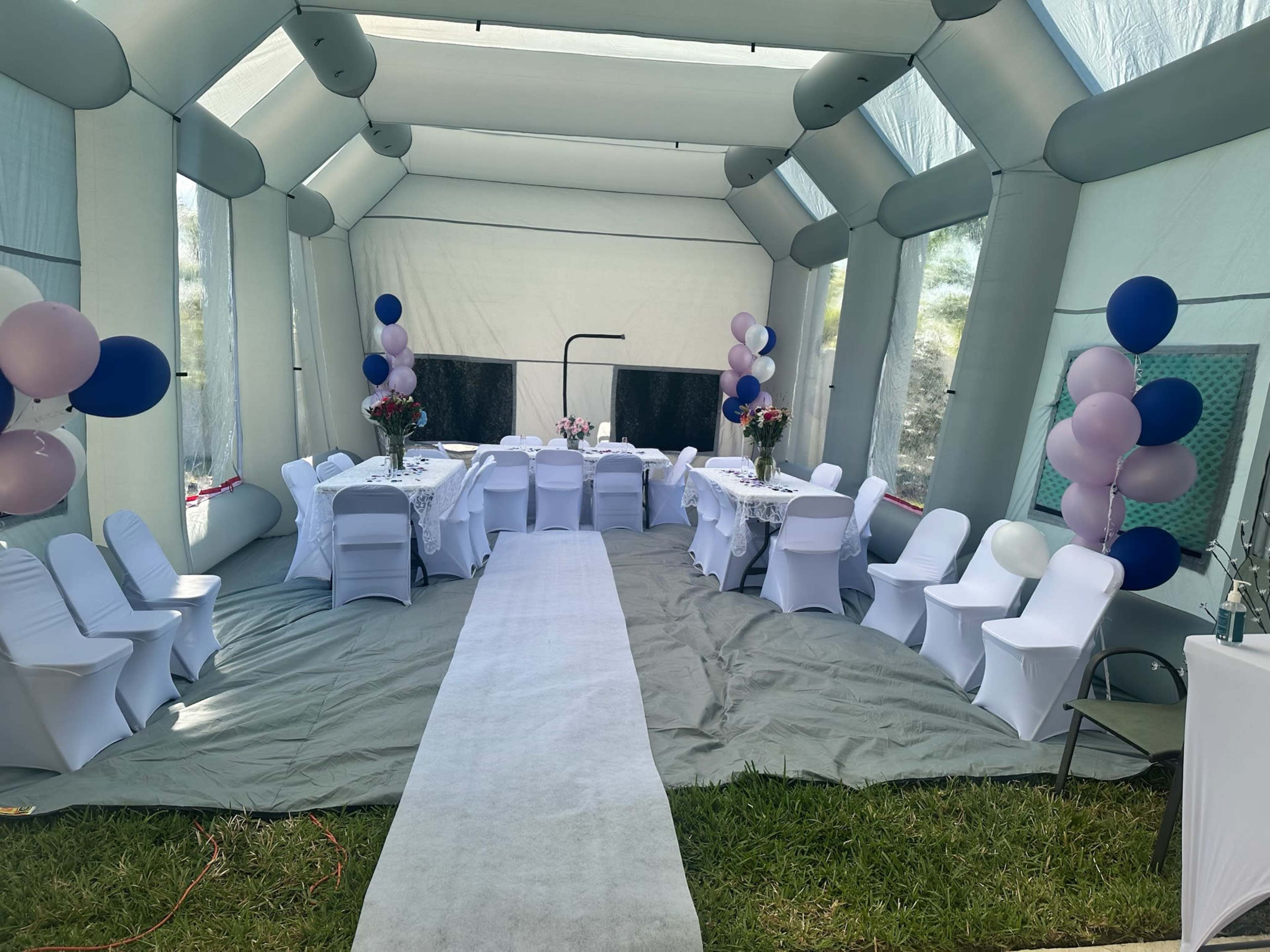 An inflatable pavilion set up for an event, featuring tables covered in white tablecloths and decorated with balloons and floral arrangements.