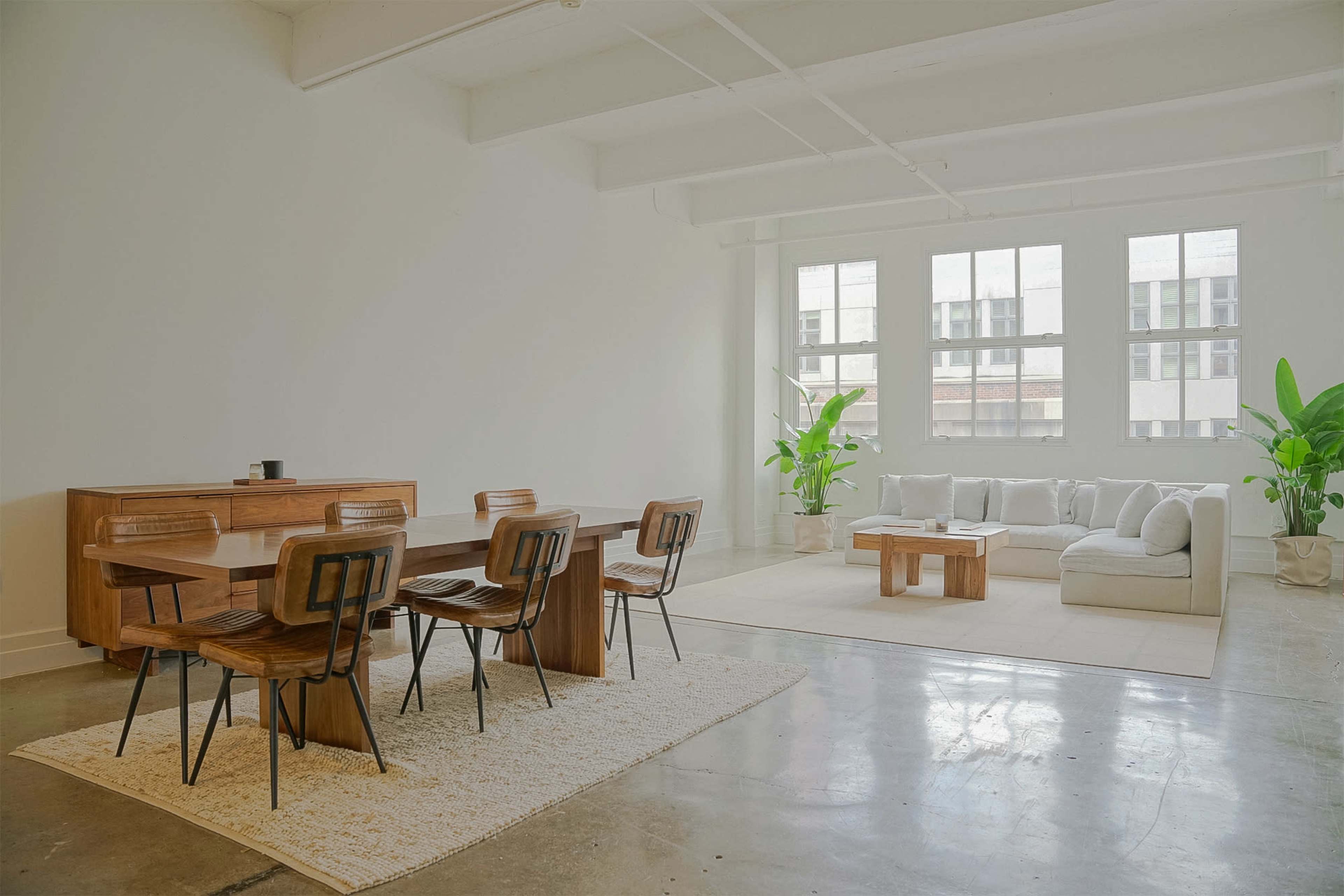 A spacious interior features a wooden dining table with chairs, a cozy seating area, and large windows allowing natural light to fill the room.