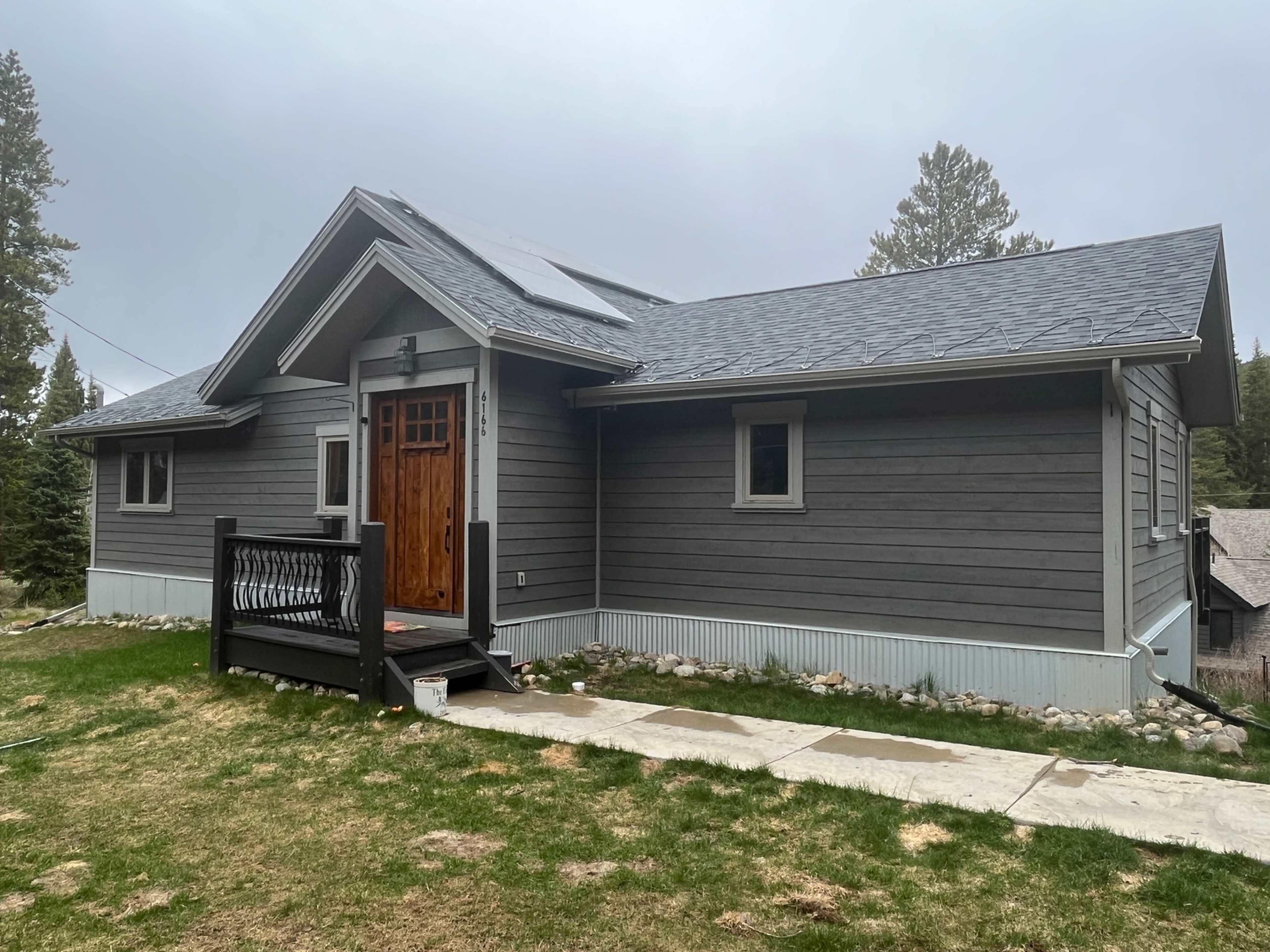 A modern gray wooden house with a sloped roof, featuring a wooden front door and a small porch.