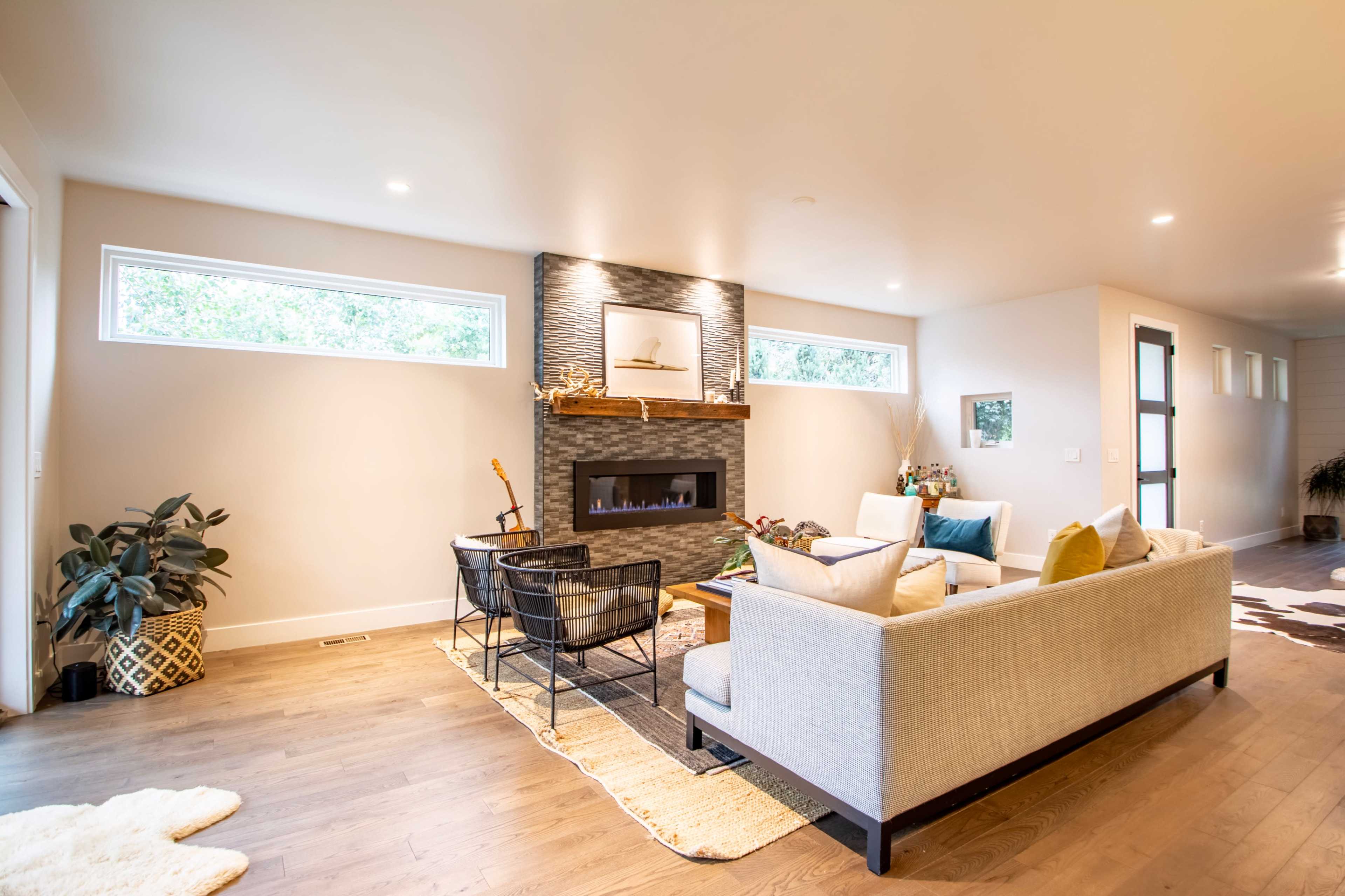 The living room features a light-colored sofa, a modern fireplace with a stone surround, and large windows allowing natural light to enter.