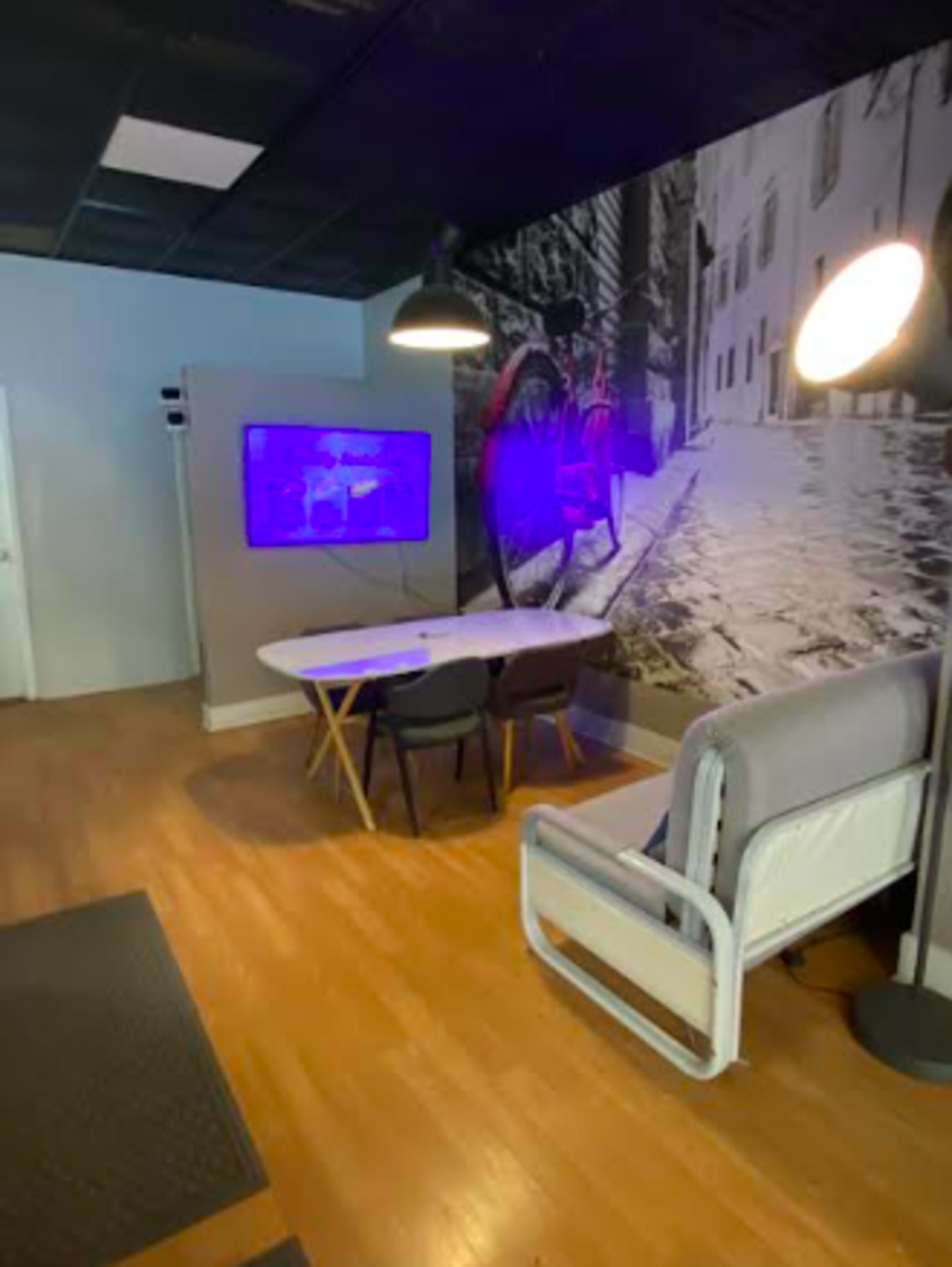 The image shows a modern office space featuring a table with chairs, a large wall mural depicting a street scene, and a floor lamp providing light.
