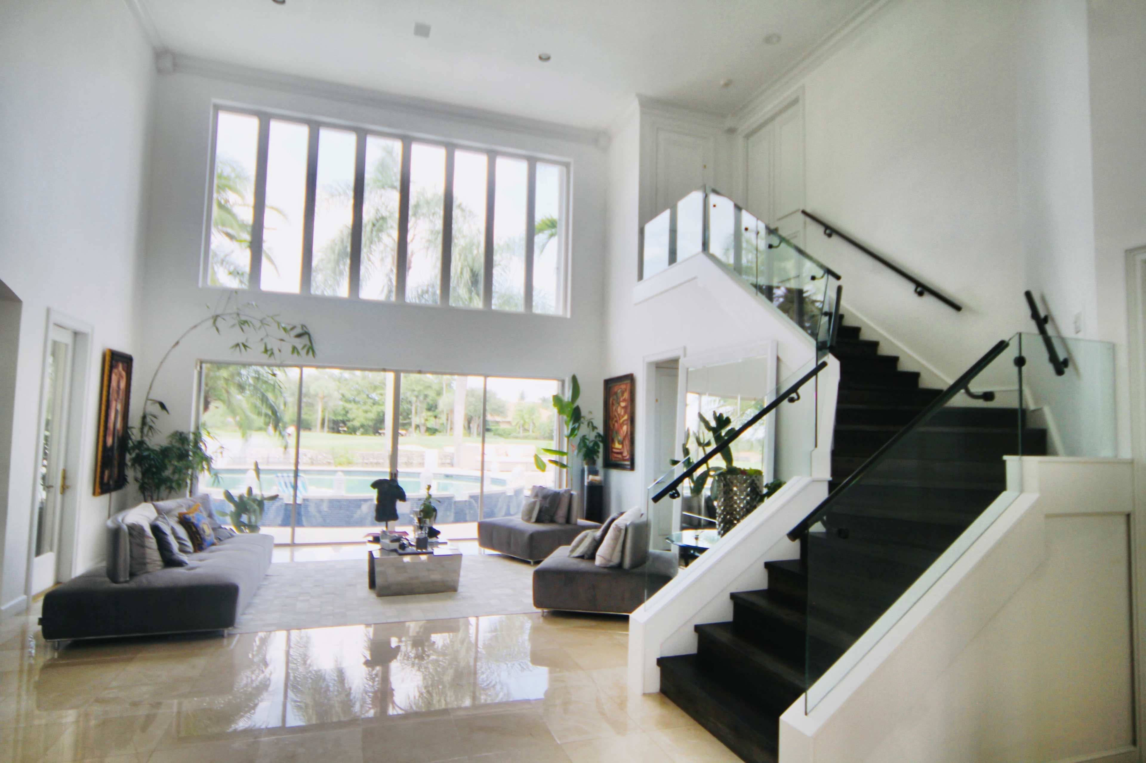A spacious, modern living room with large windows, a staircase leading to an upper level, and elegant seating arrangements.