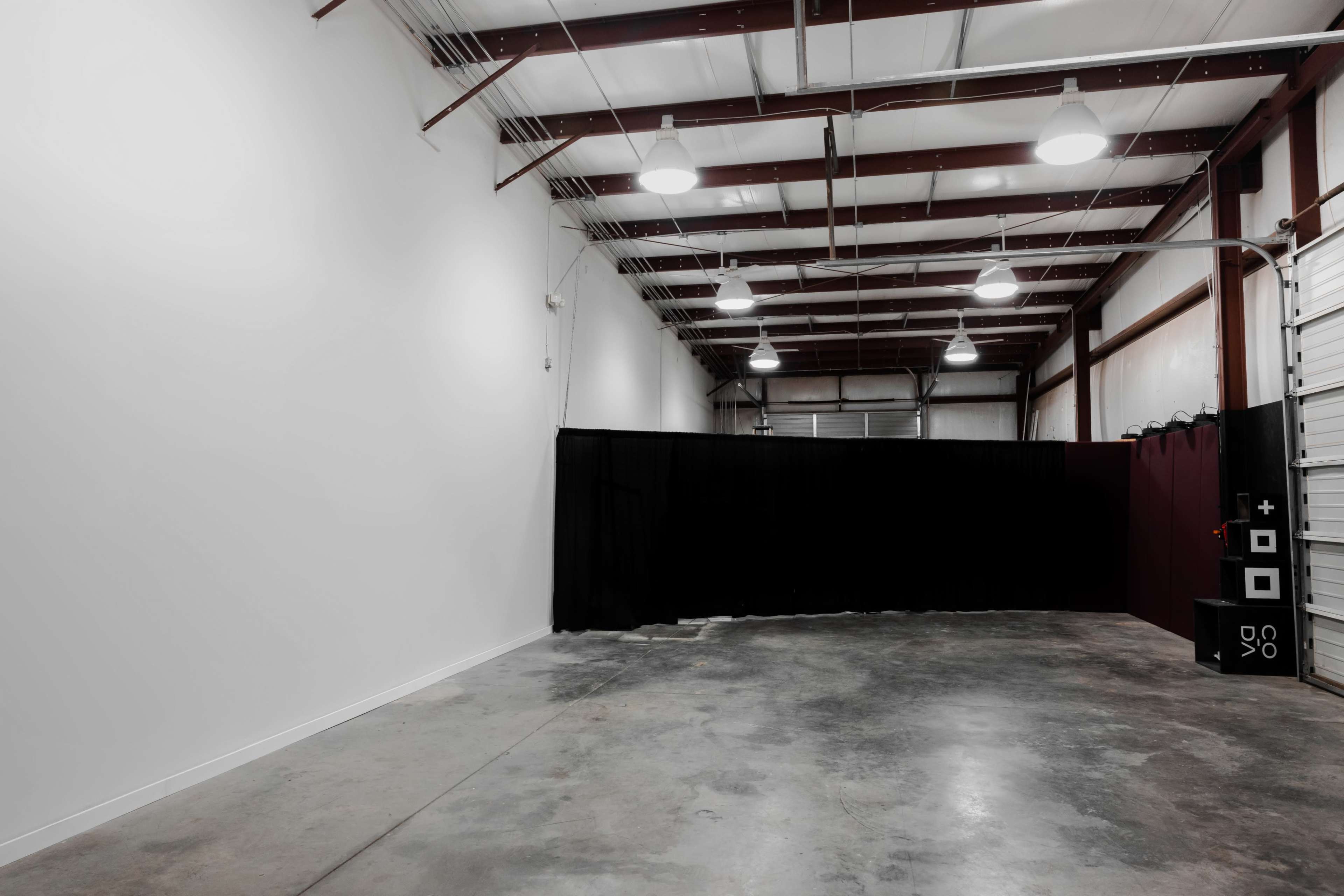 An empty industrial space with a concrete floor, high ceilings, and a dark curtain at one end.