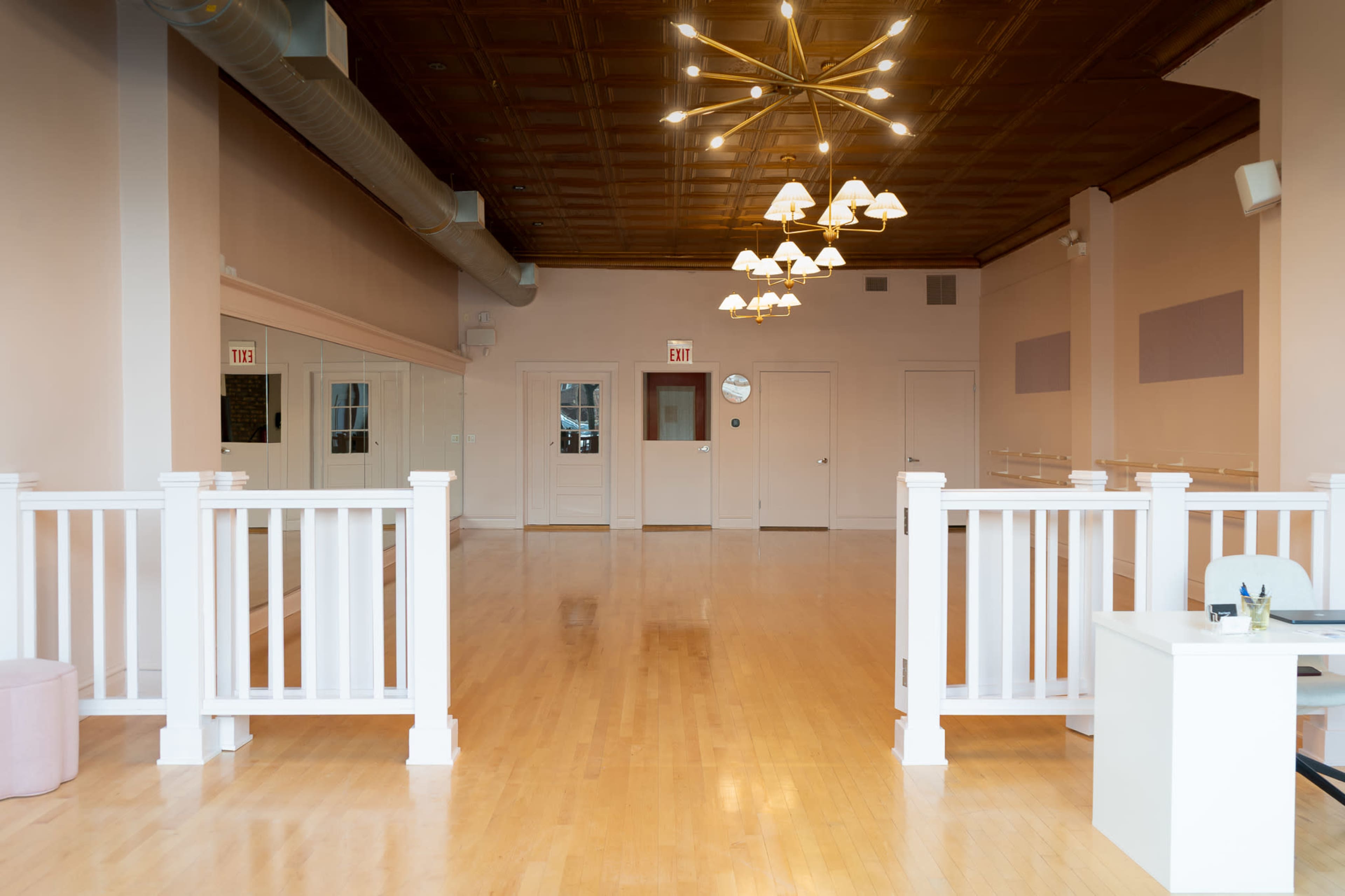 The image shows a spacious, well-lit interior featuring hardwood flooring, white railings, and a decorative ceiling light fixture.