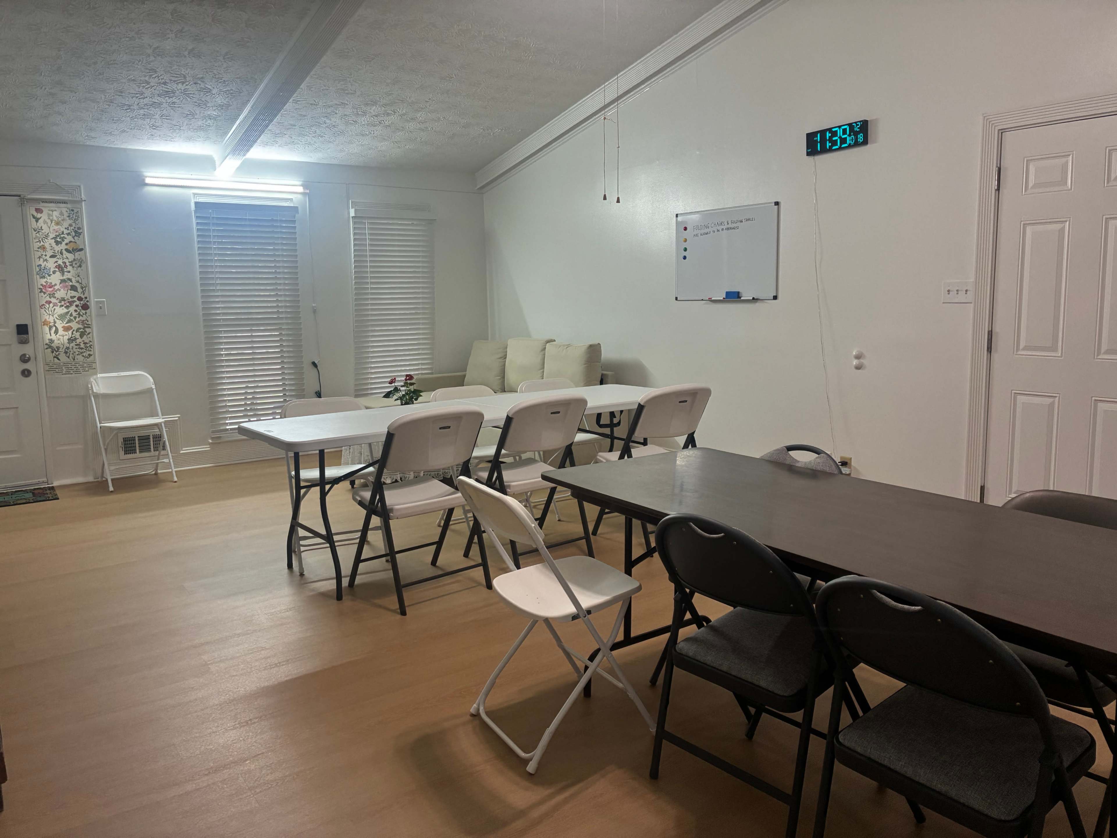 The image shows a spacious room with two tables arranged for meetings, several chairs around the tables, and a whiteboard mounted on the wall.