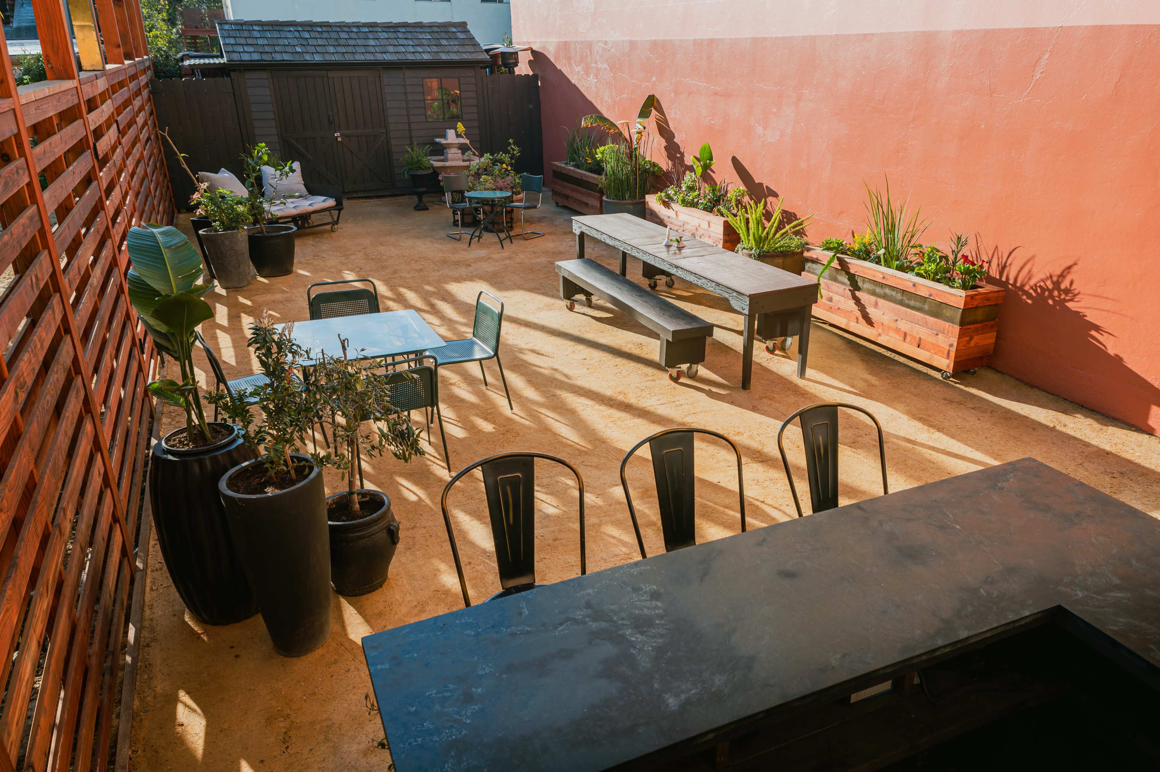 A landscaped outdoor space featuring various seating areas, planters, and several tables surrounded by greenery.