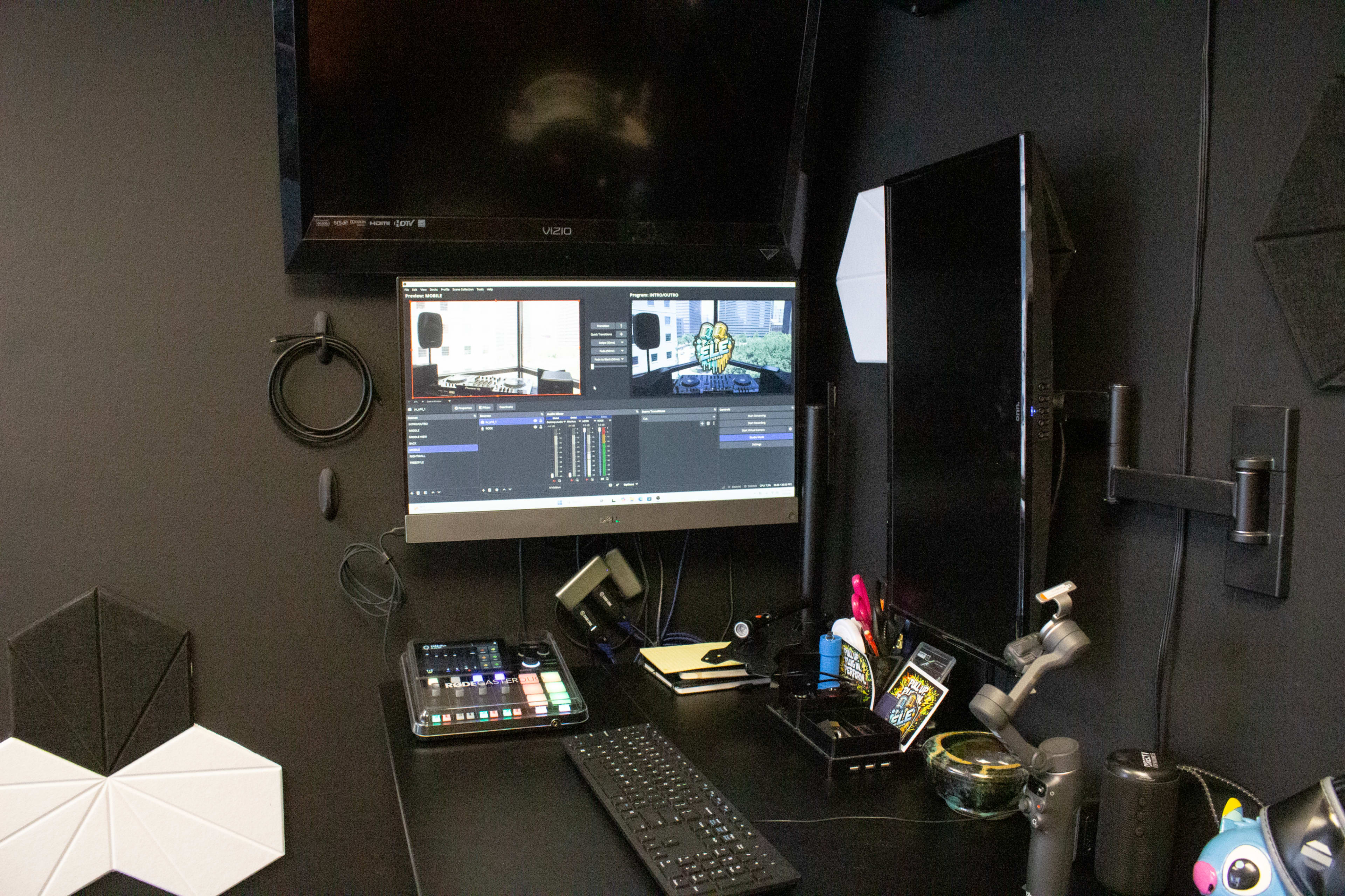 The image shows a modern computer workspace with a large monitor displaying video editing software, a keyboard, and various tools neatly arranged on a black desk.