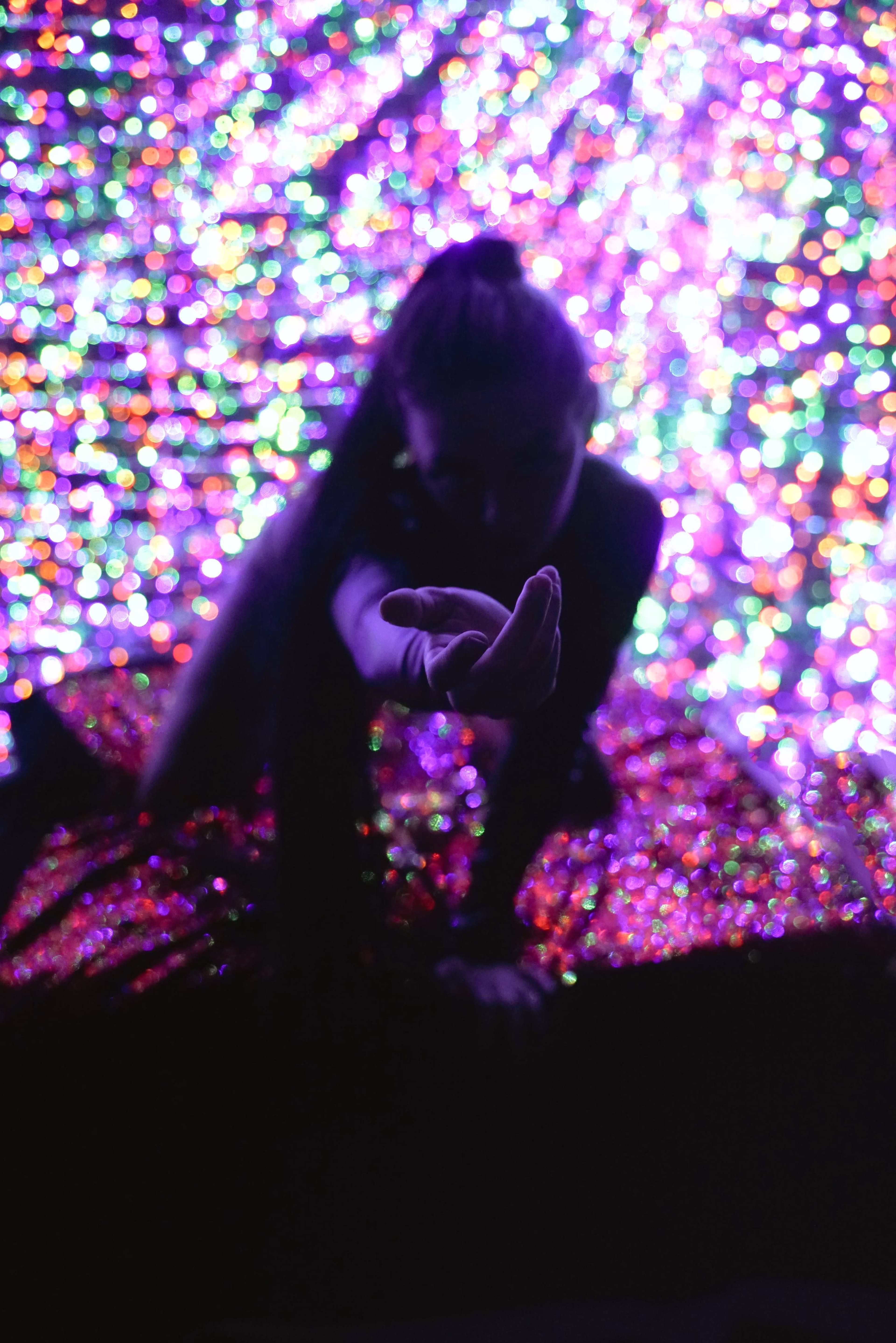 A person reaches toward the camera while surrounded by a vibrant, colorful backdrop of lights.
