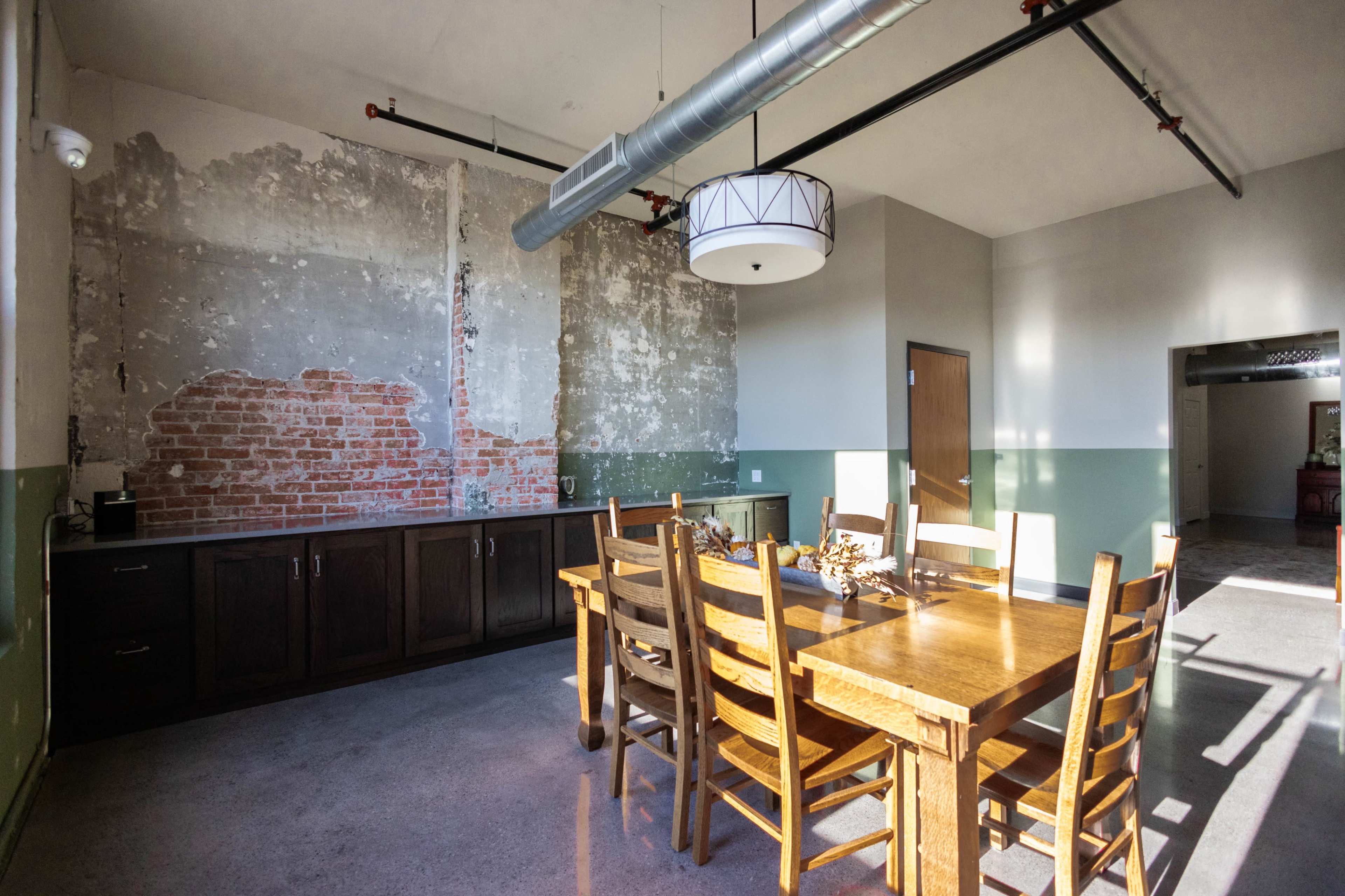A dining area features a wooden table with chairs, adjacent to a wall with exposed brick and a painted green lower section.