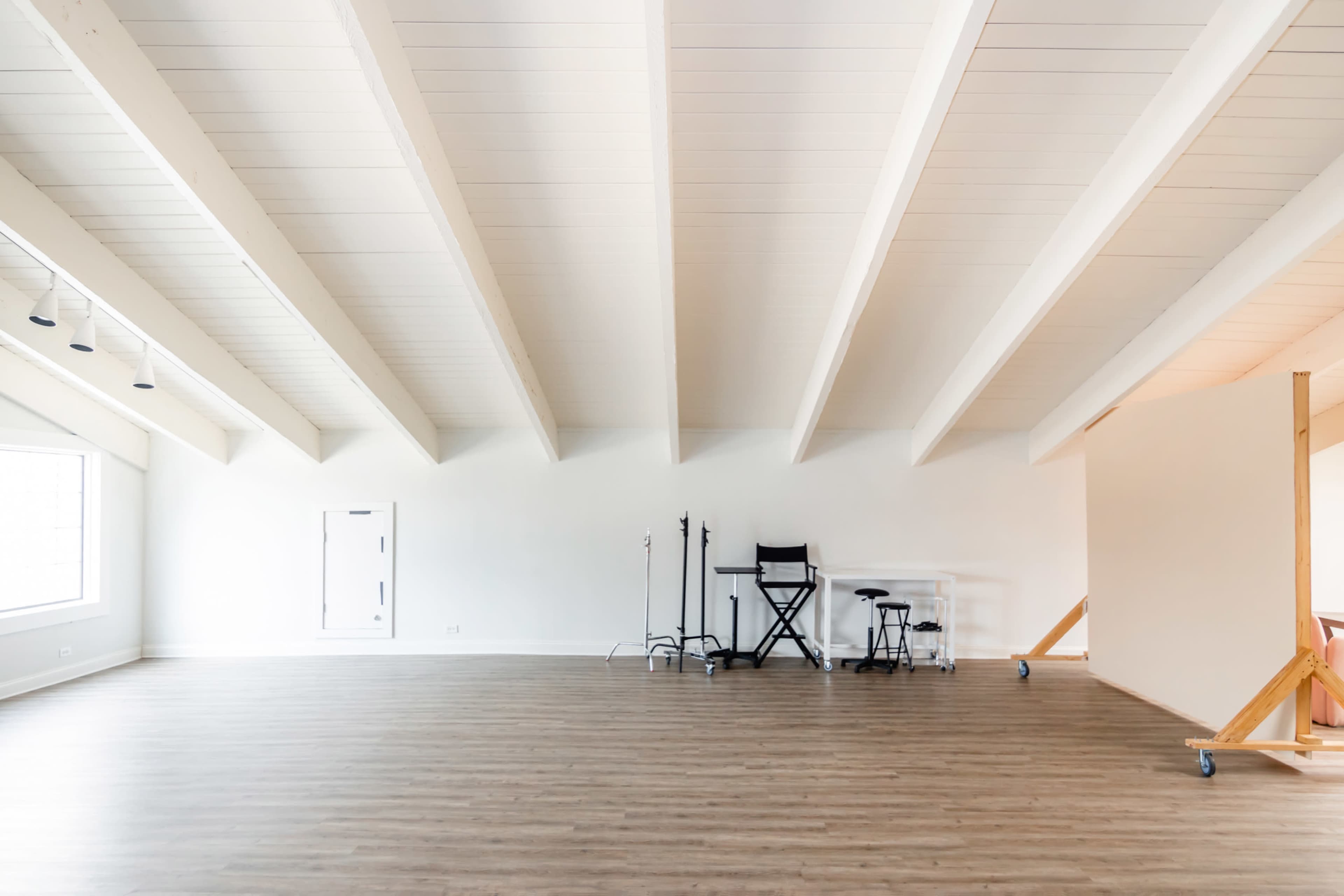 A spacious, empty room with high wooden beams and minimal furniture, including a black chair and a small table against one wall.