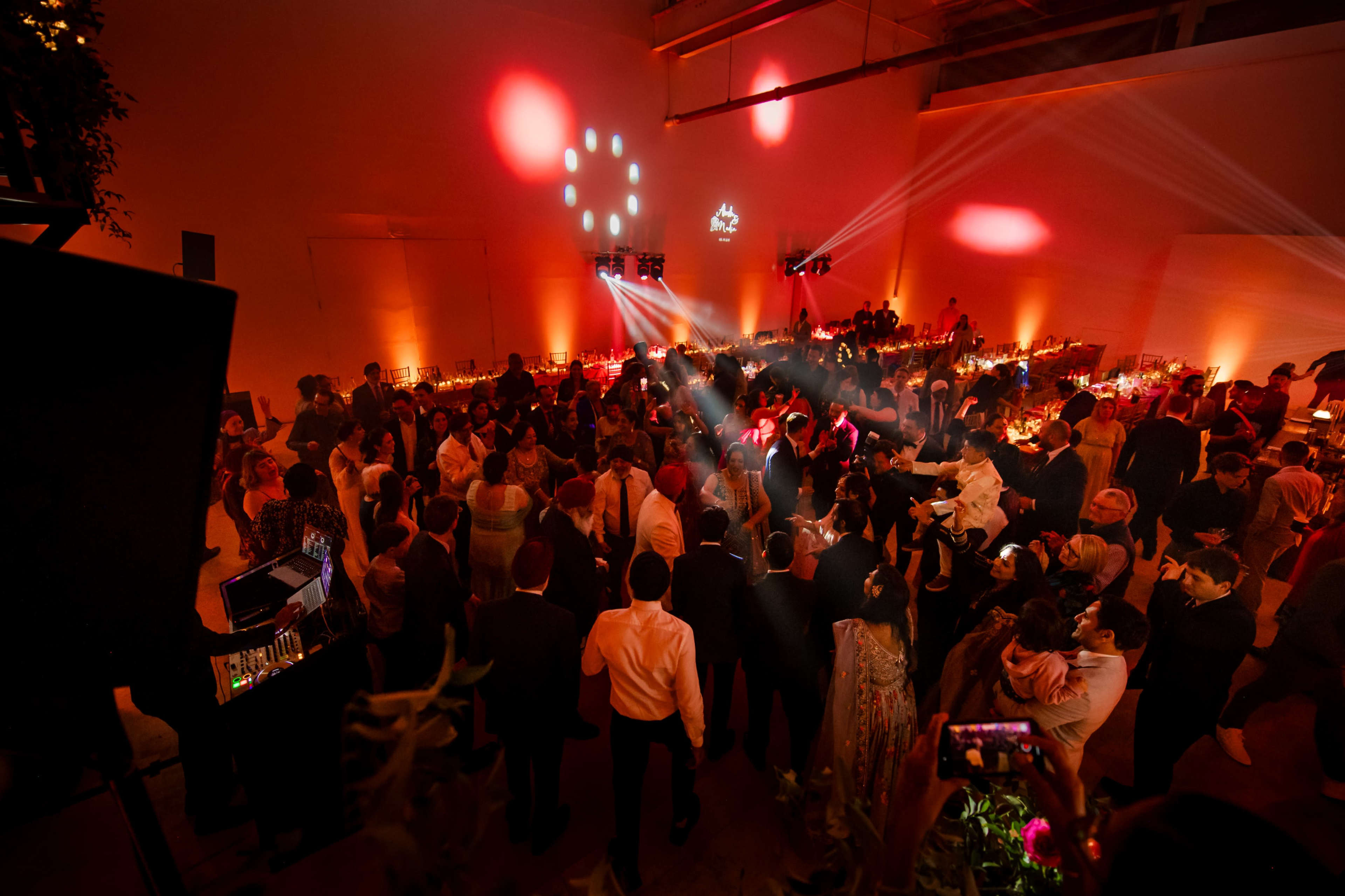 A large crowd gathers to dance and celebrate at a brightly lit event with colorful lights and decorations.