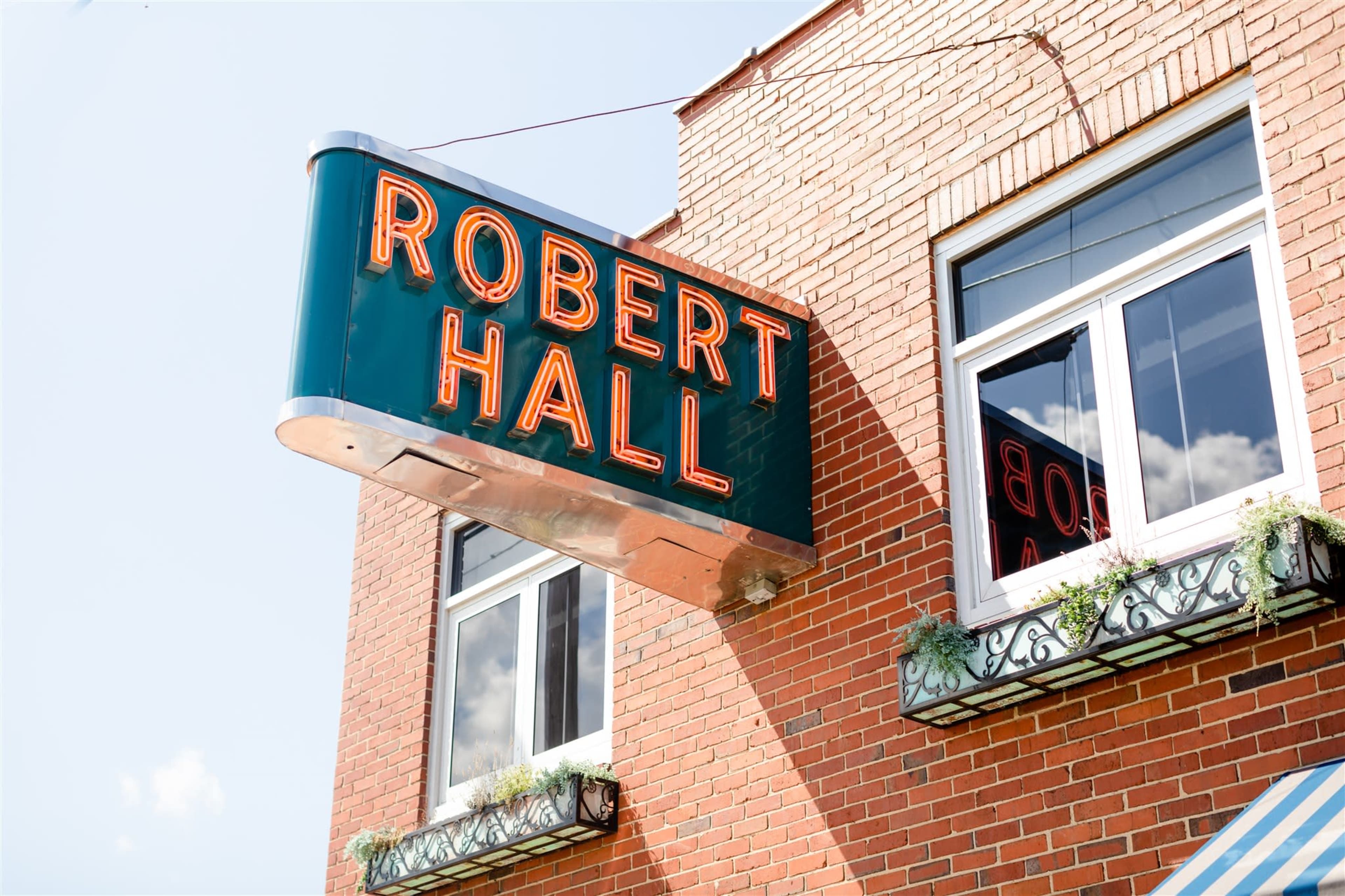 A neon sign reading "ROBERT HALL" is mounted above a brick building with windows and decorative planters.