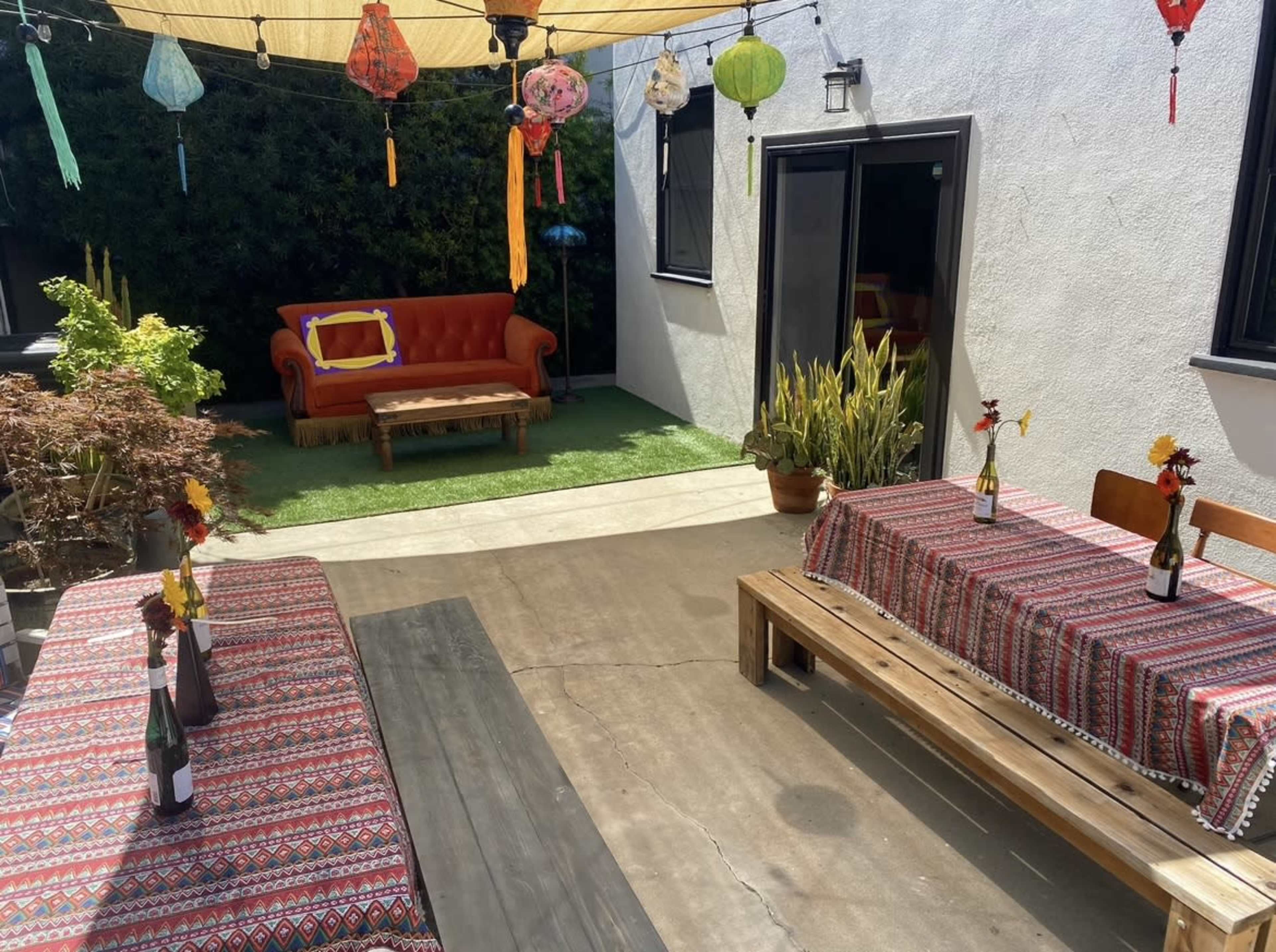 The outdoor space features two tables with decorative table settings, a red couch, potted plants, and colorful lanterns overhead.