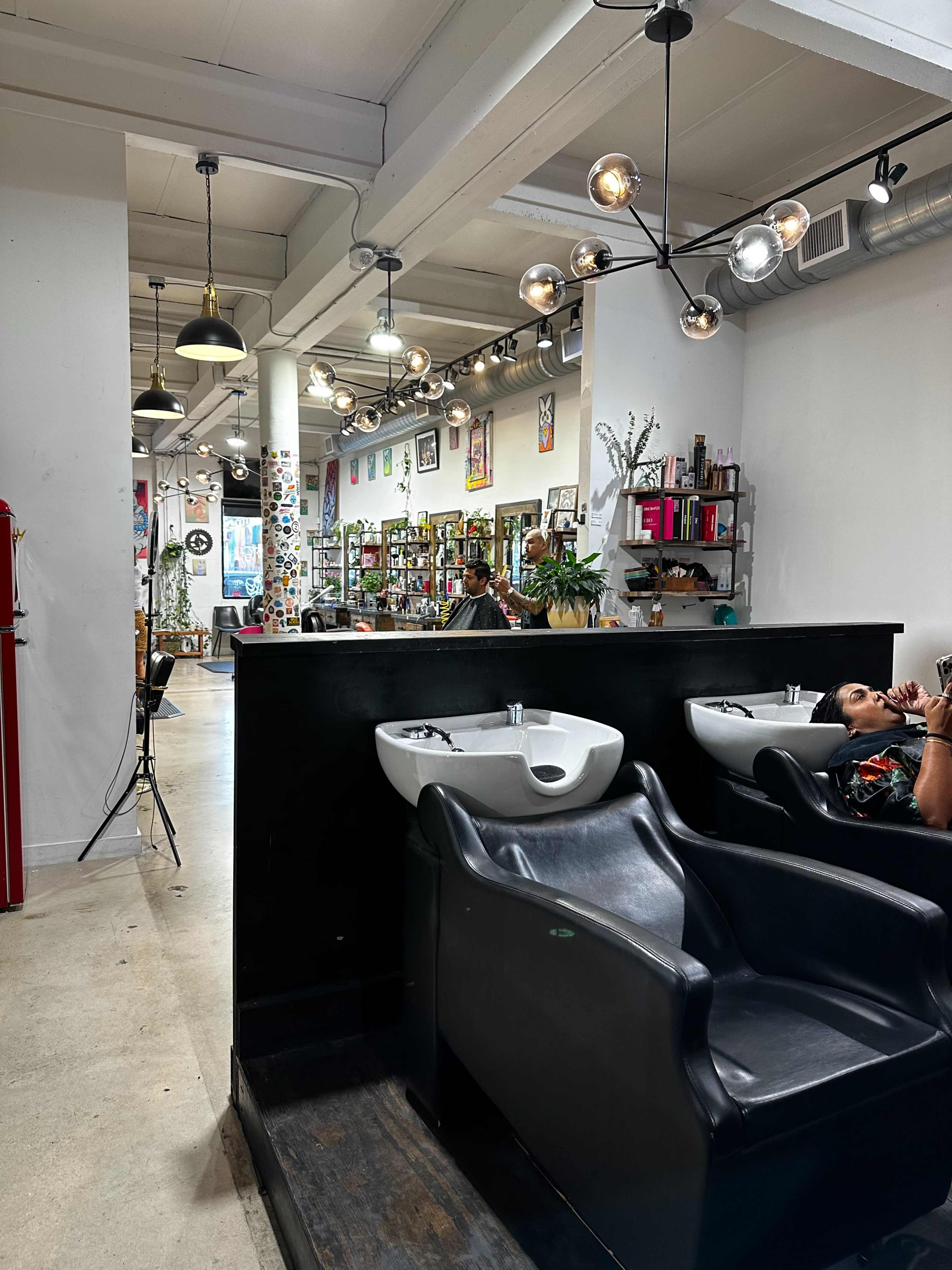 The image shows a modern salon interior with hair washing stations in the foreground and various beauty products displayed on shelves in the background.