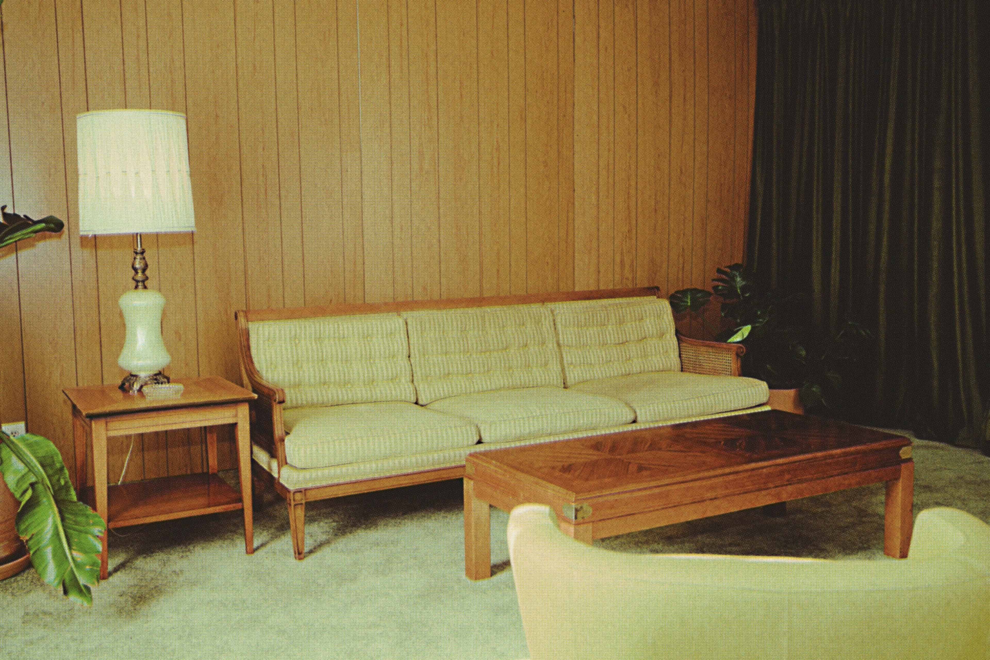 A minimalist living room featuring a striped sofa, a wooden coffee table, and a tall lamp beside a small side table, with a backdrop of wood paneling and green curtains.