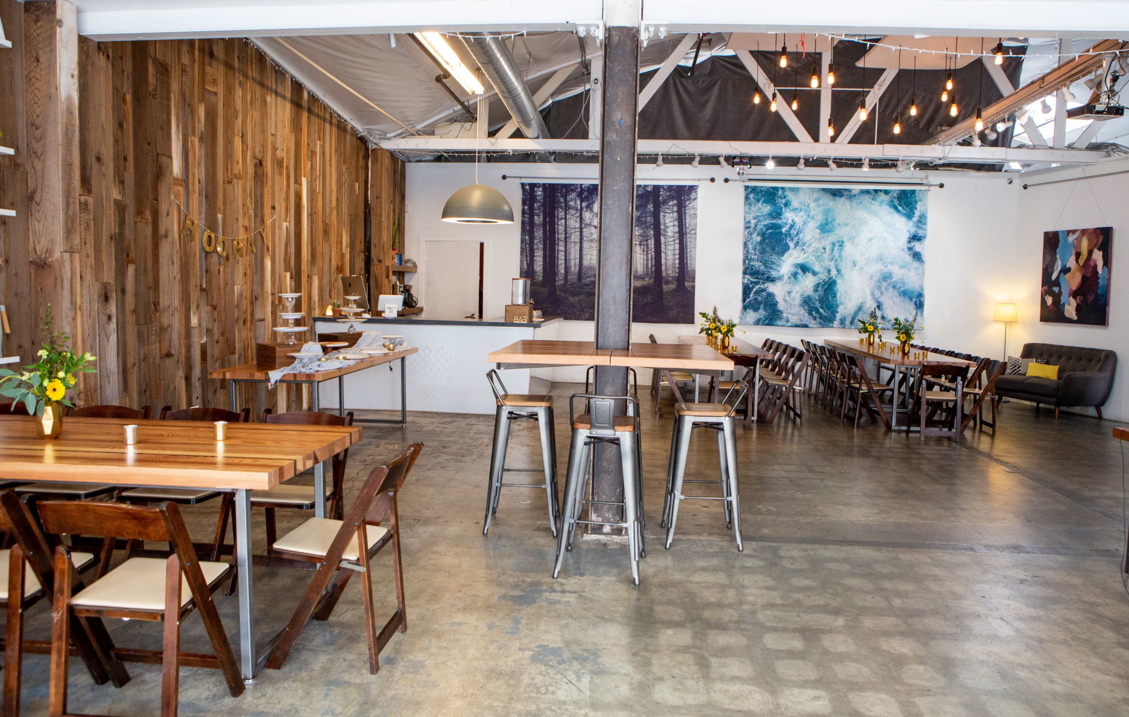An interior space of a modern café featuring wooden walls, multiple seating areas with tables and chairs, and large wall art depicting nature themes.