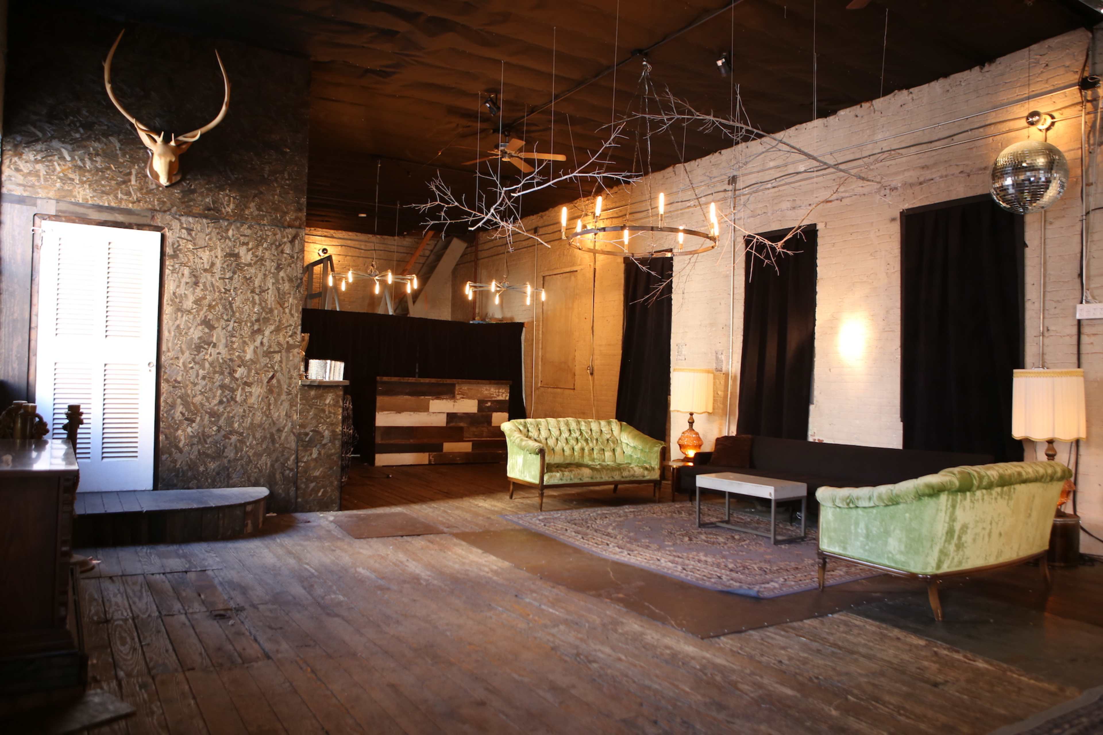 A spacious room with rustic decor, featuring two green velvet sofas, a wooden coffee table, and various hanging light fixtures.
