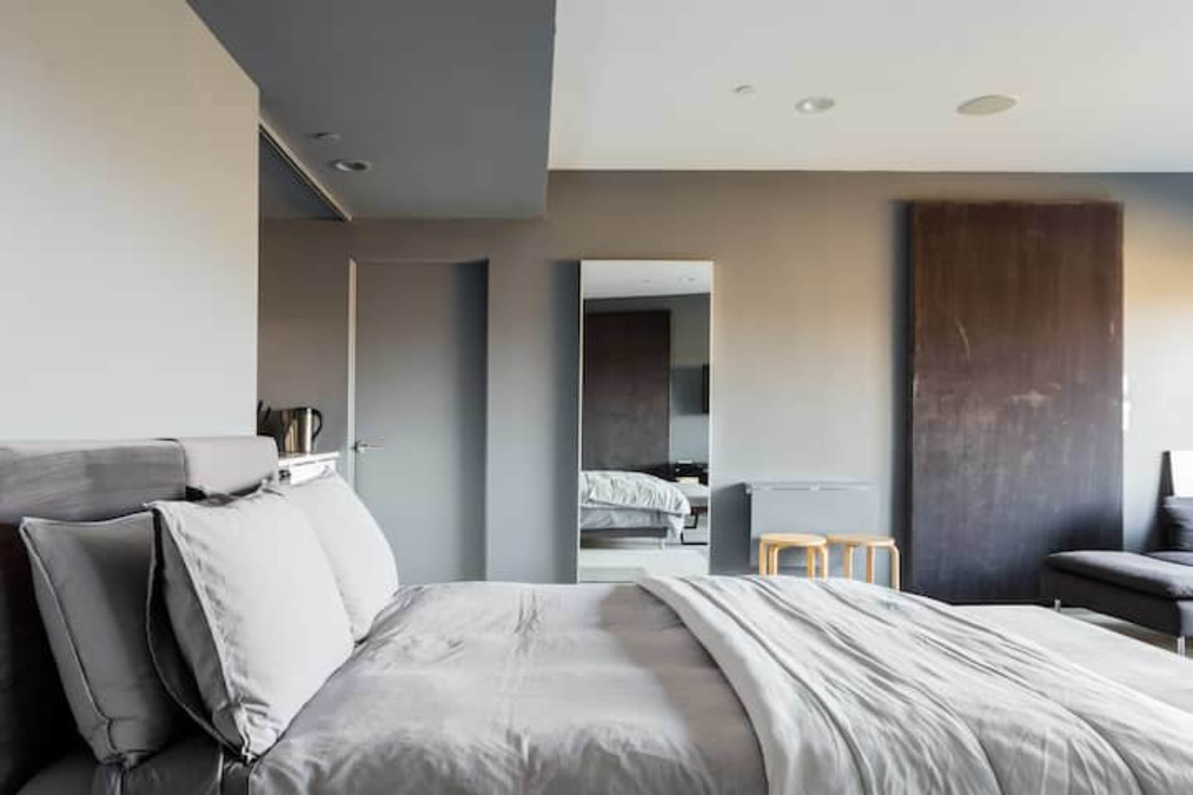 A modern bedroom features a bed with gray bedding, a large mirror, and minimalist furniture.