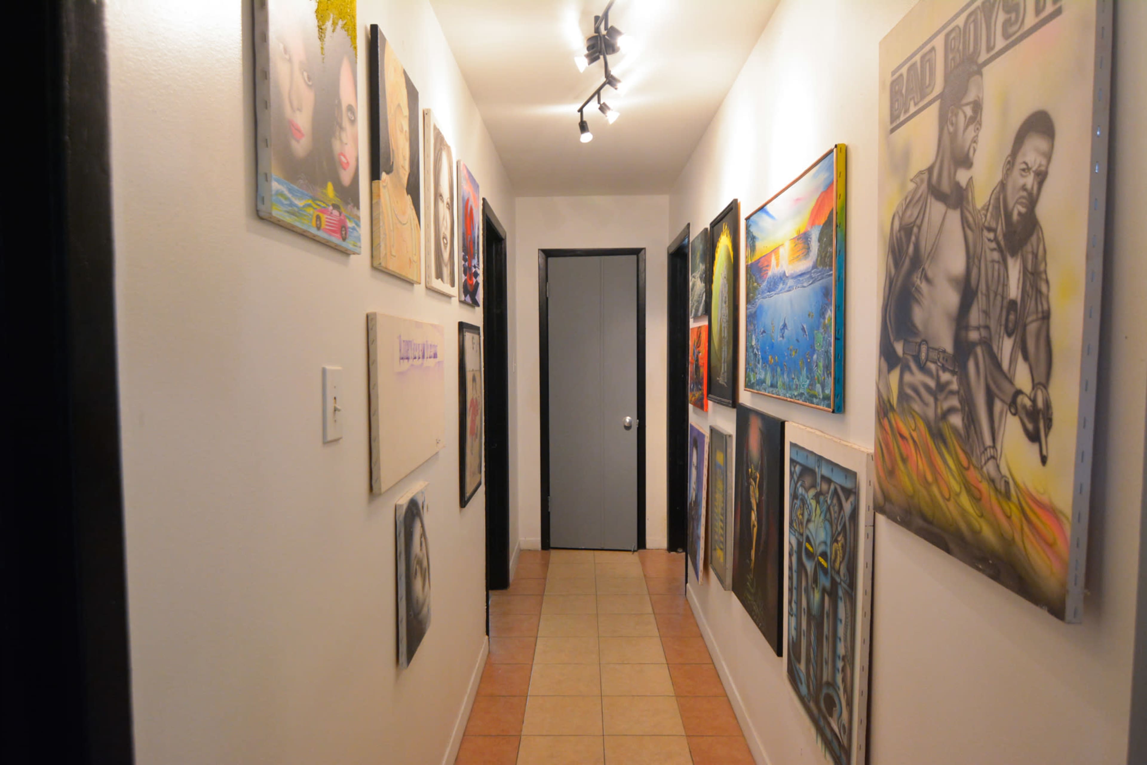 A narrow hallway features framed artworks hung on both sides, leading to a closed door at the end.