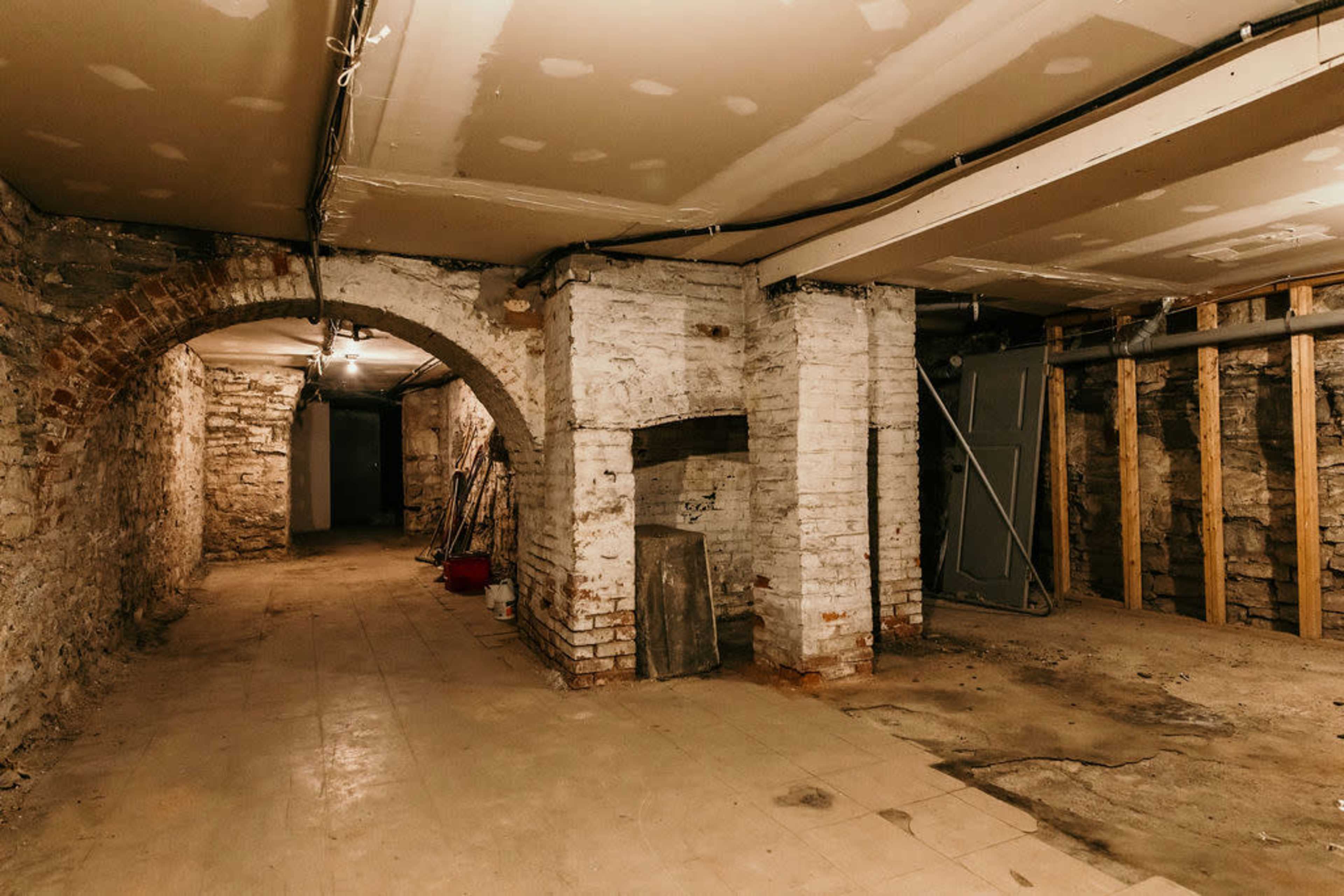 A dimly lit basement with exposed brick walls, archways, and scattered construction materials.