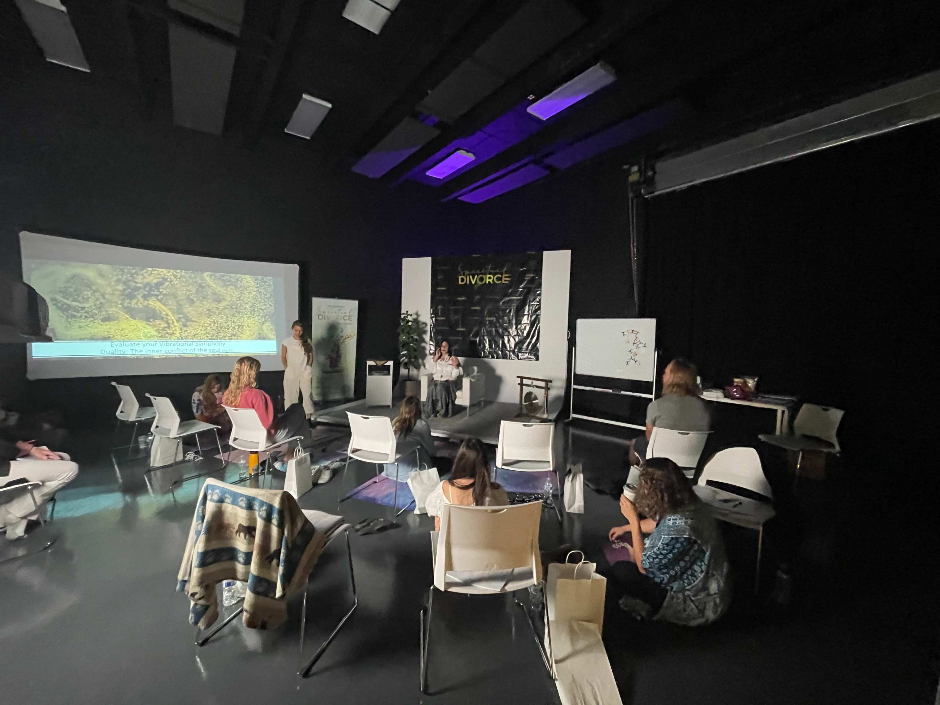 A group of people is seated in a room, facing a presentation screen, while a few individuals participate in a discussion at the front.